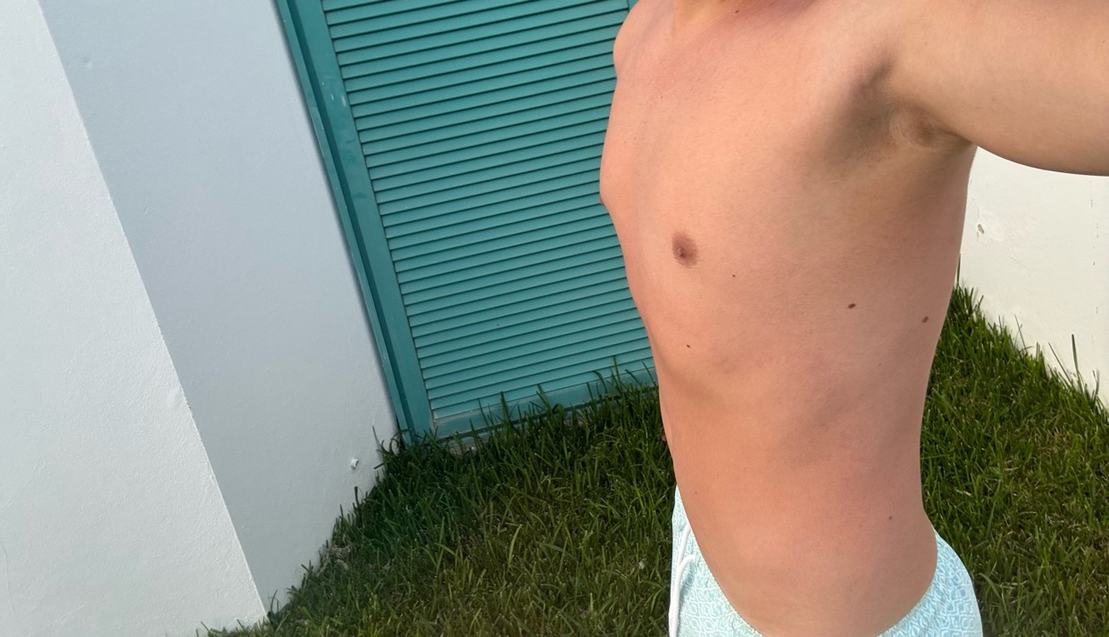A man is shown from the chest down, wearing light blue swim trunks. He has visible tan lines on his torso, suggesting he has been in the sun.