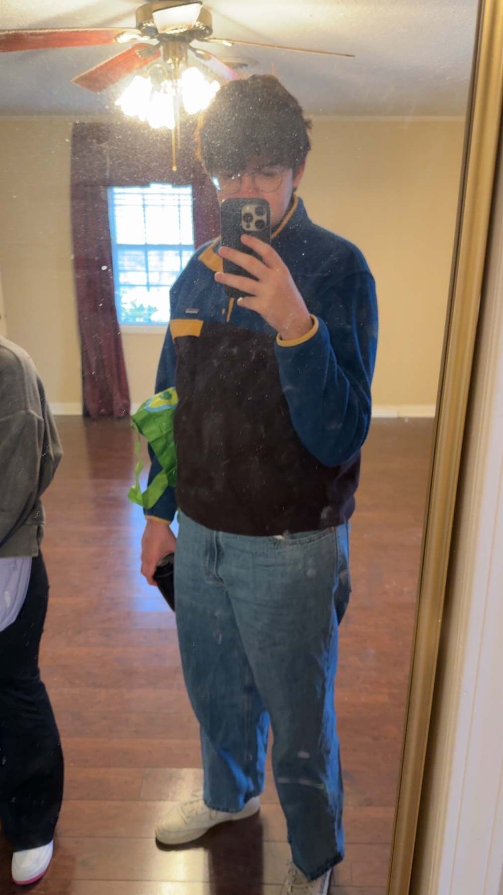 A man takes a mirror selfie, showcasing his outfit. He's wearing jeans, a jacket, and sneakers.