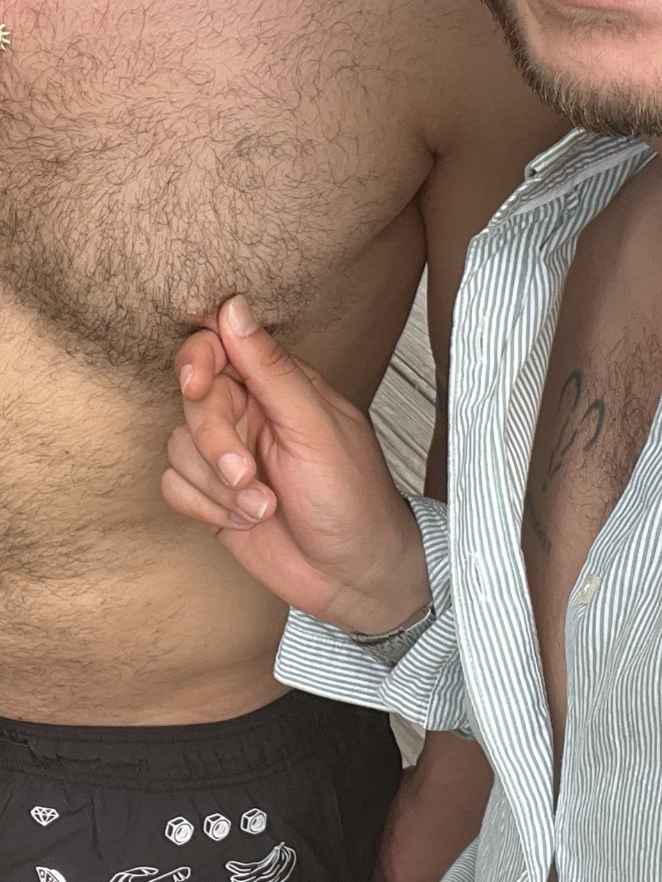 A close-up photo of two men, one shirtless and the other wearing a partially unbuttoned striped shirt. They are embracing.