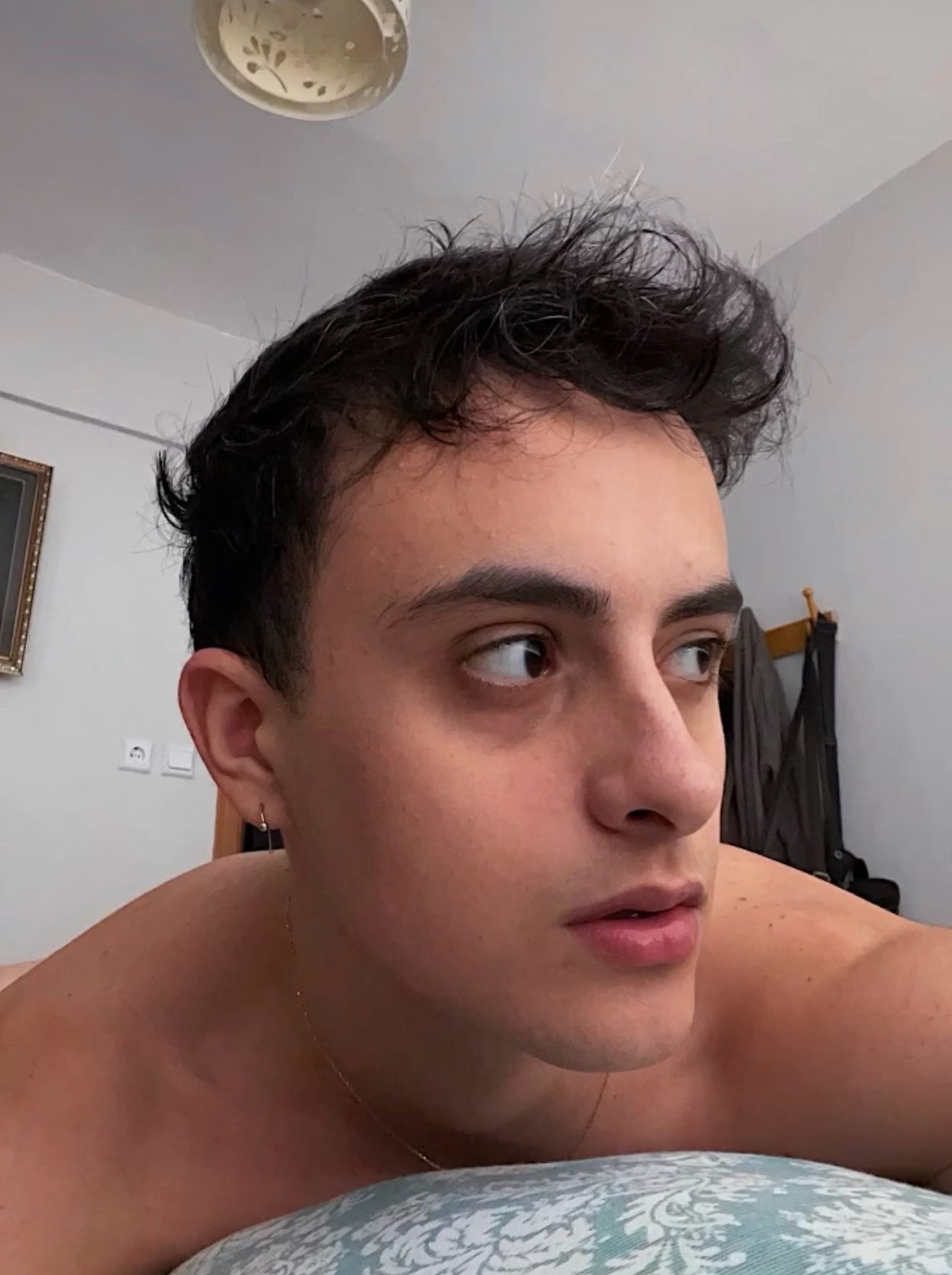 A man is lying down and looking away from the camera. The photo is a selfie taken indoors.