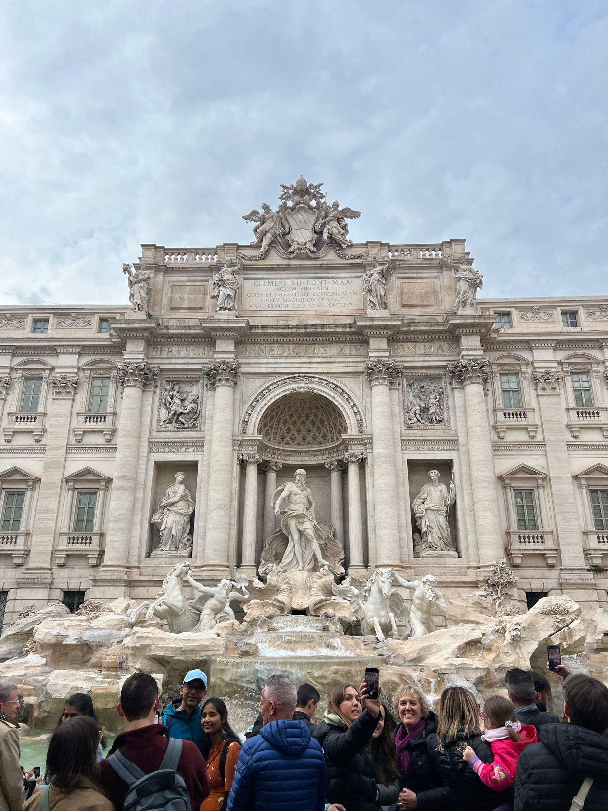 A crowd of tourists gathers in front of the magnificent Trevi Fountain in Rome, Italy. The Baroque fountain, adorned with intricate sculptures and a grand facade, is a popular landmark.