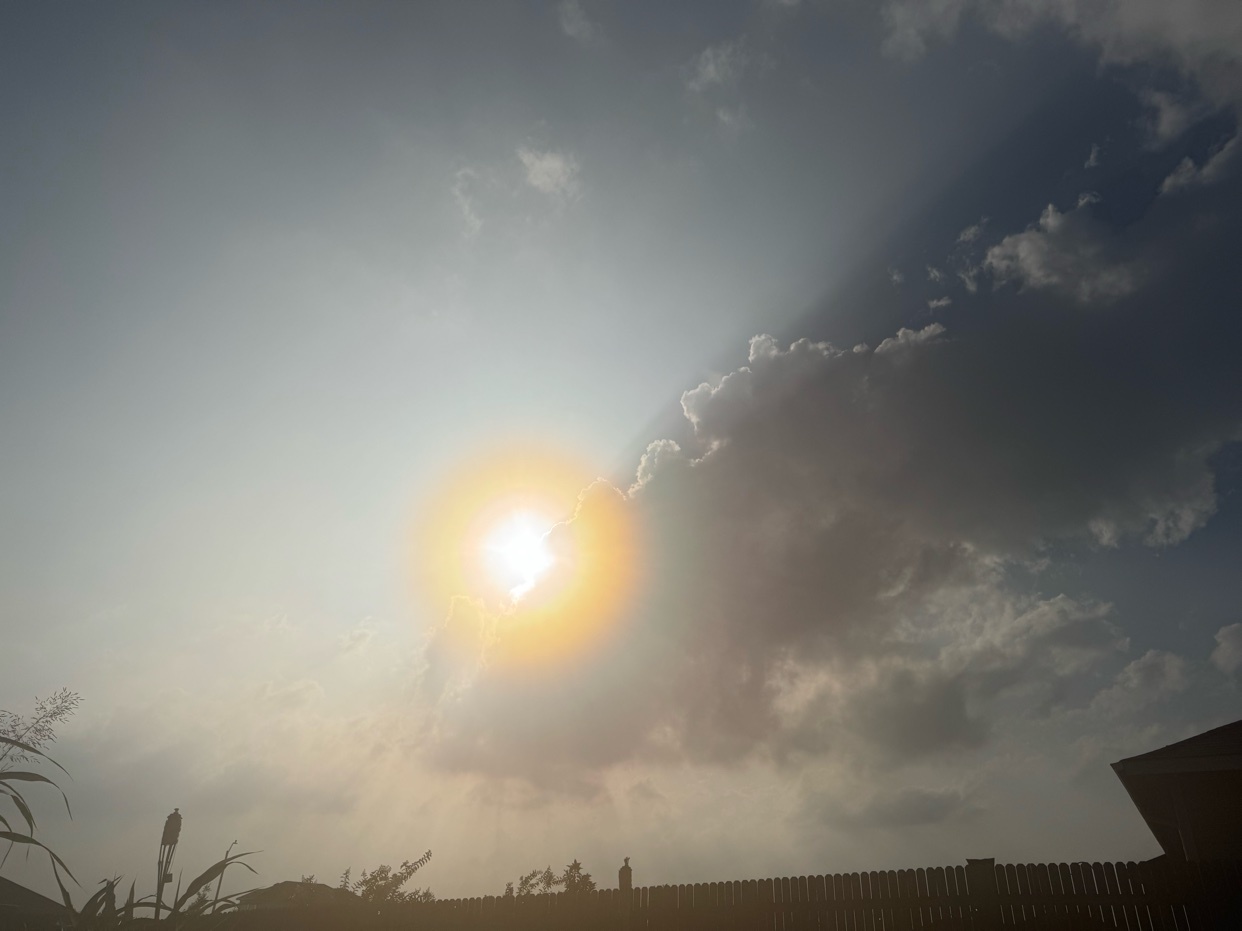 The sun shines brightly through a gap in the clouds, casting dramatic rays across the sky. The scene captures a beautiful moment of natural light and weather.