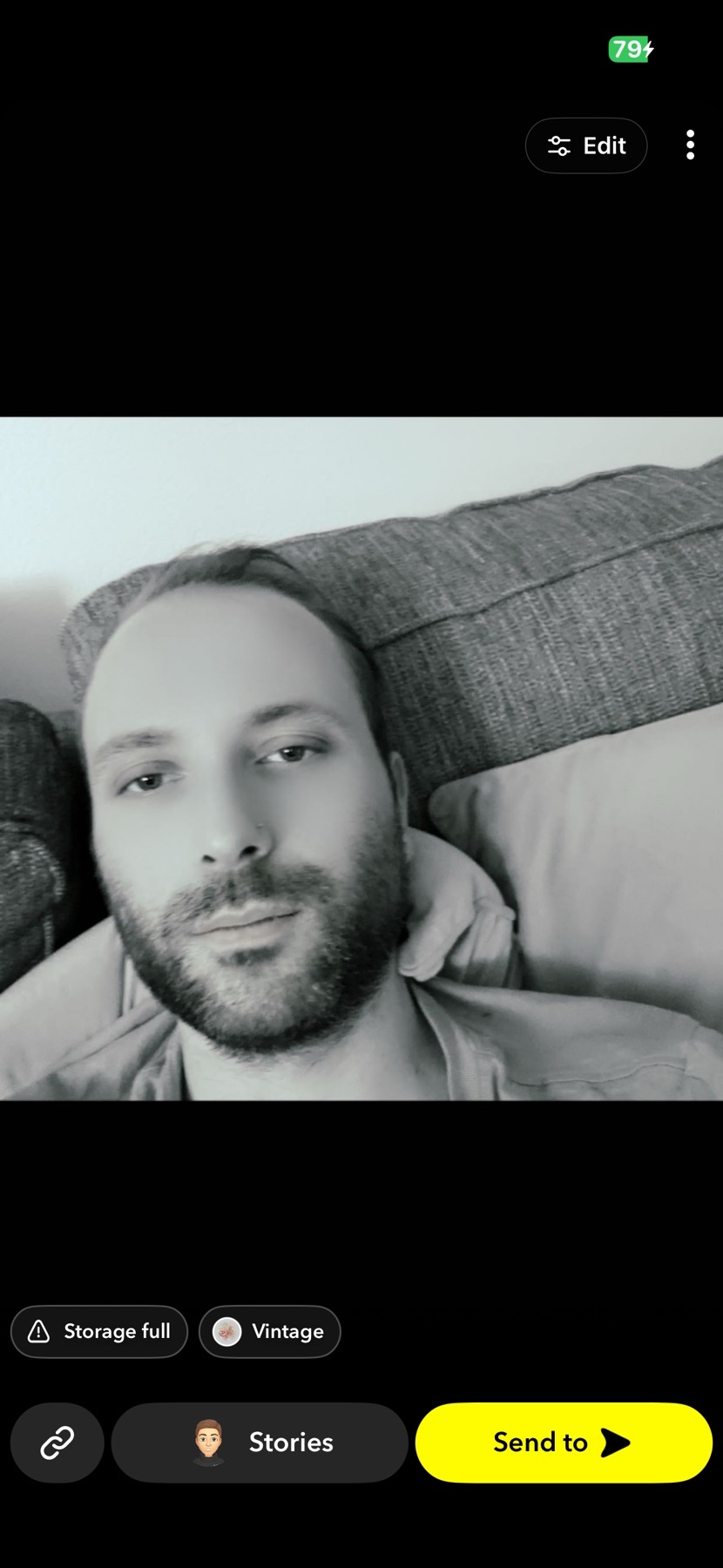 A black and white selfie of a man with a beard and stubble, looking directly at the camera while lying down.