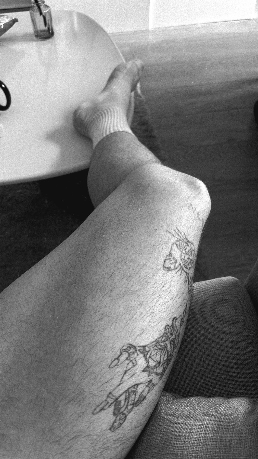 A black and white close-up of a person's leg with a tattoo of a skeleton hand.