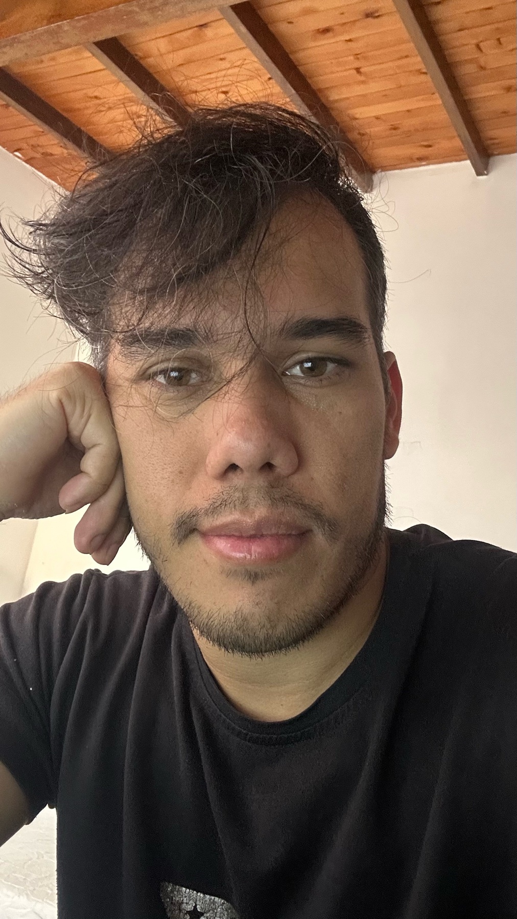 A close-up selfie of a man with dark hair and stubble, resting his head on his hand.