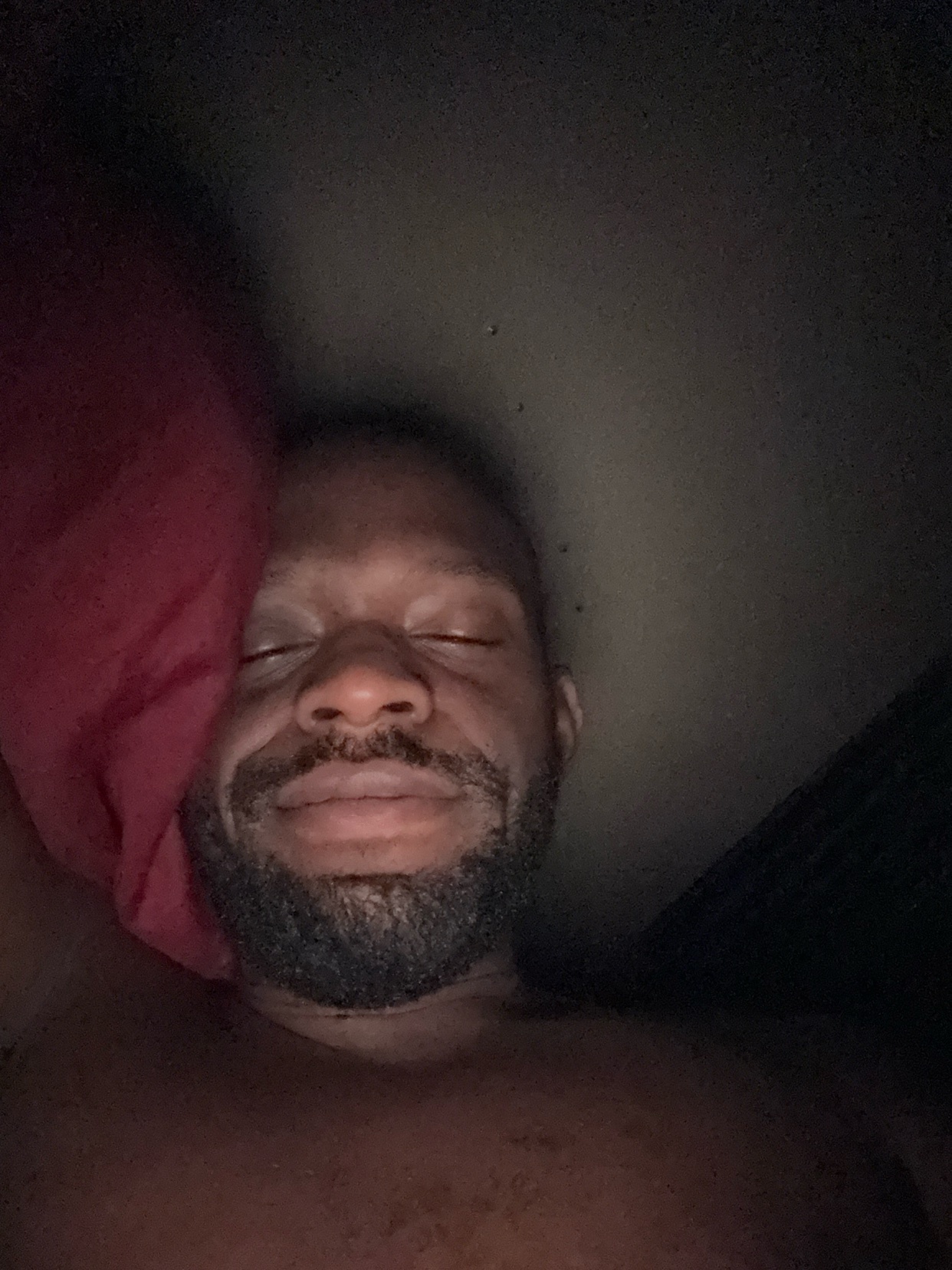 A man is lying down with his eyes closed. The image is dark, and the man is shirtless.