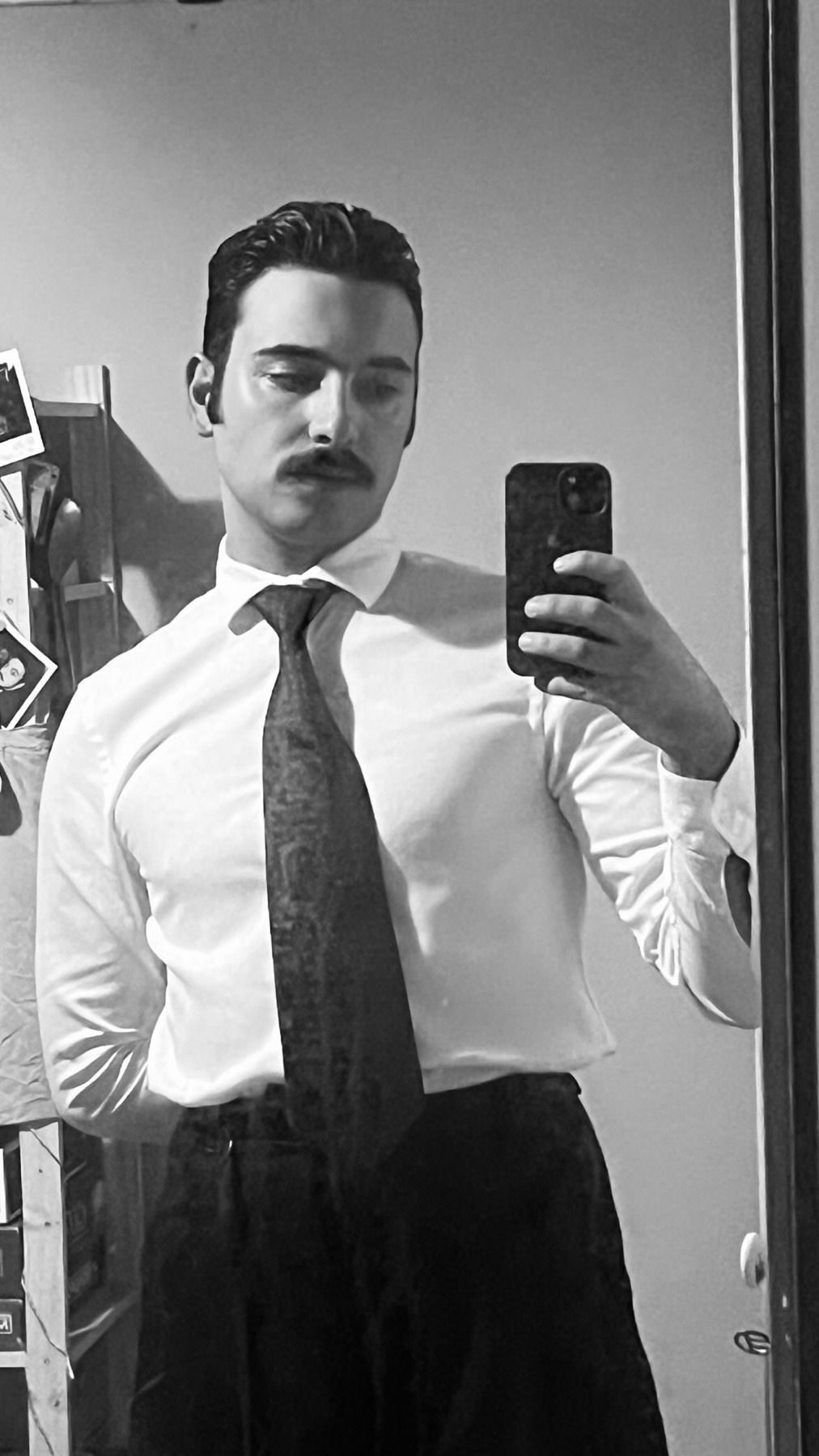 A black and white selfie of a man with a mustache wearing a collared shirt and tie.