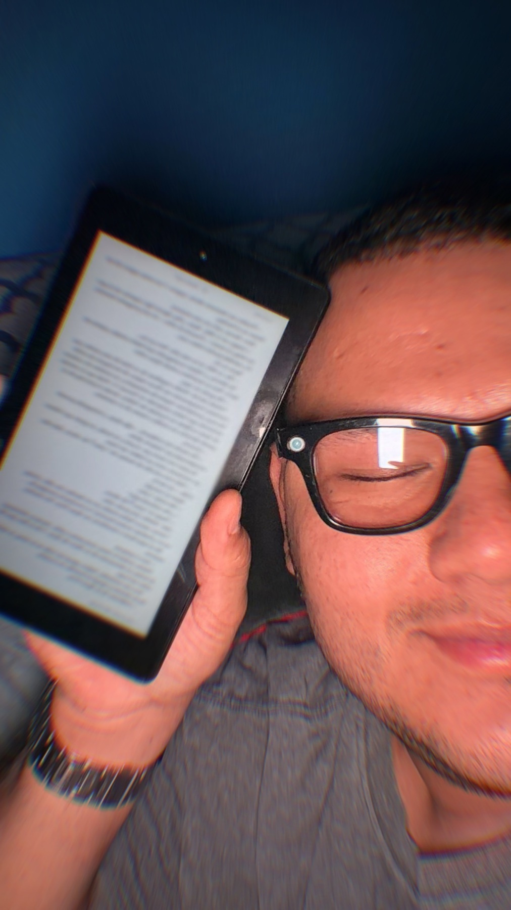 A man is holding an e-reader up to his face. He is wearing glasses and appears to be reading.