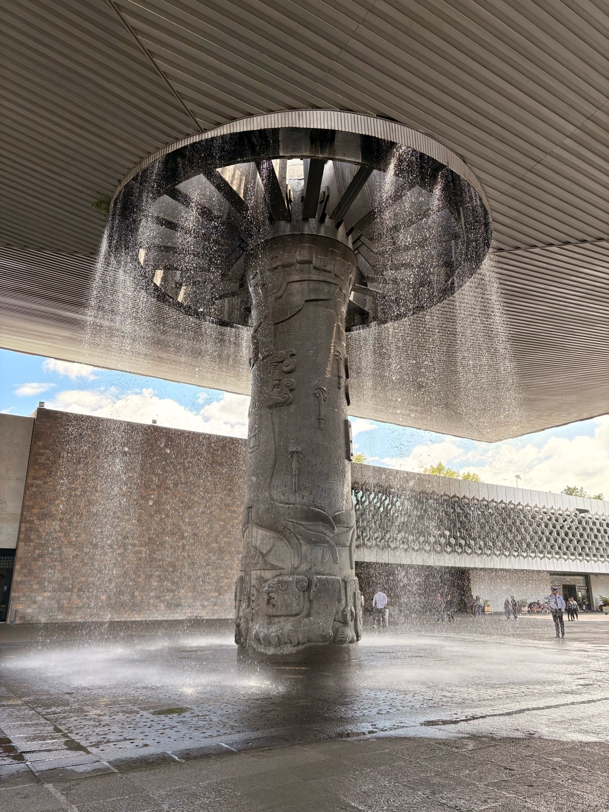 A unique fountain with water cascading from a circular structure. The fountain is a striking architectural element in an urban setting.