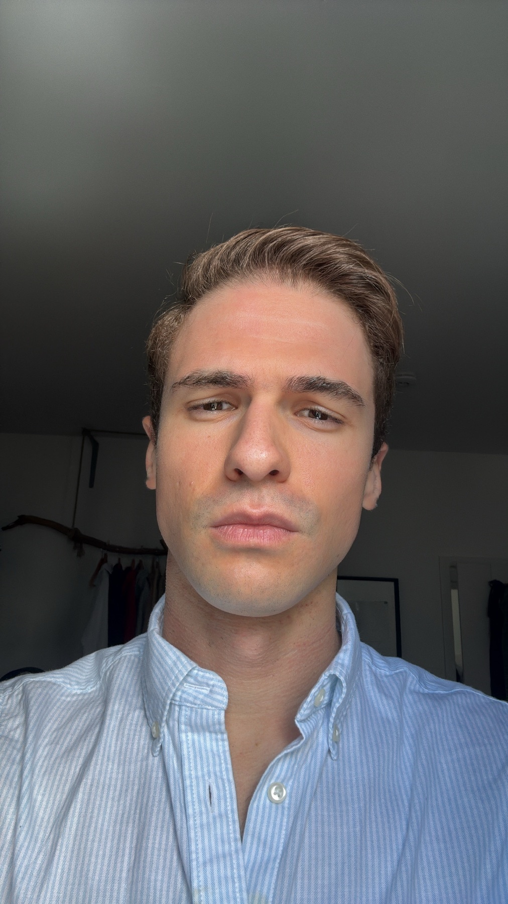 A man poses for a selfie, looking directly at the camera. He is wearing a button-up shirt and has blonde hair.