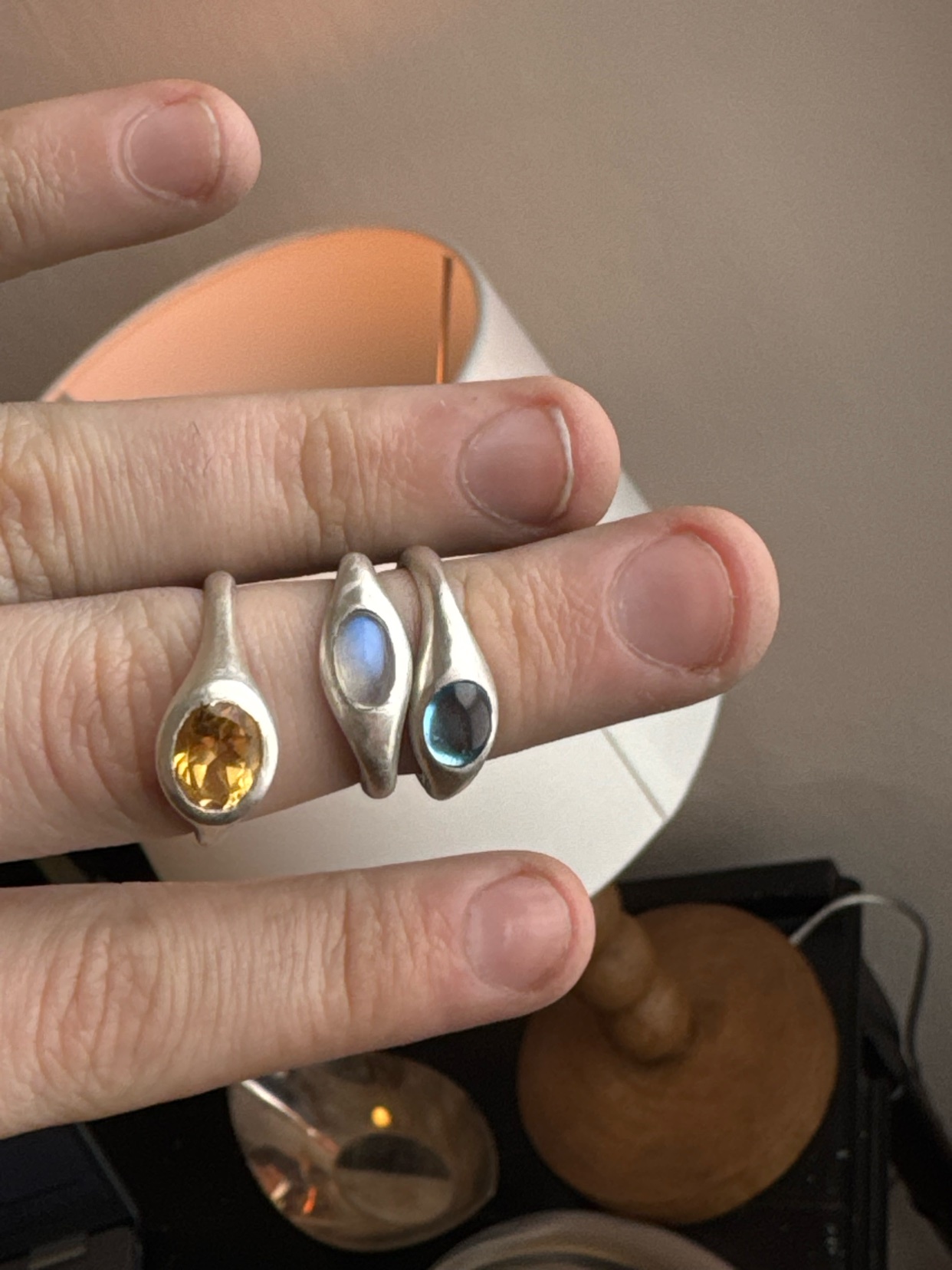 A close-up shot showcases three rings with different gemstones on a person's fingers. The rings are silver, and the gemstones include citrine, moonstone, and topaz.
