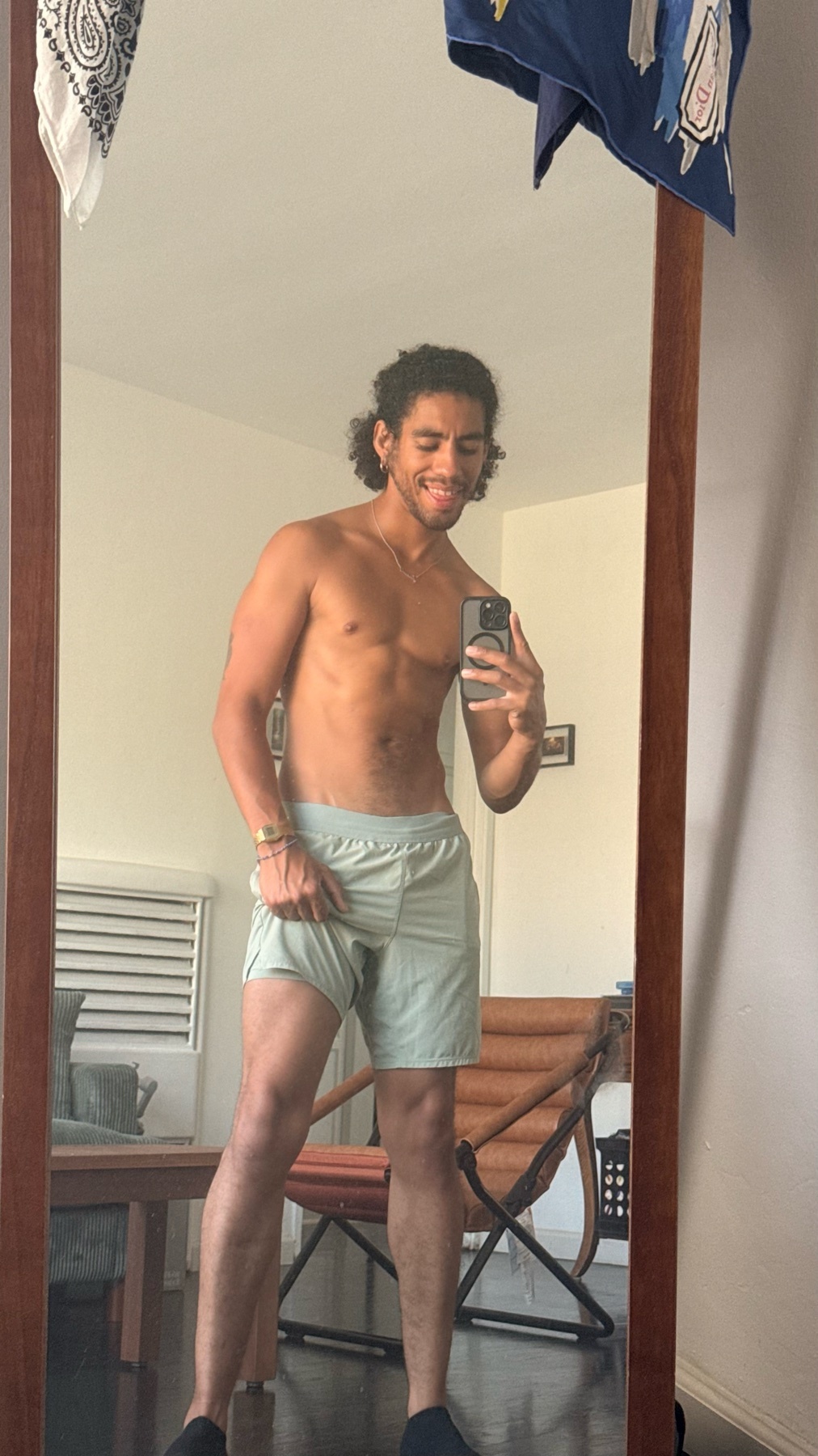 A man takes a mirror selfie while wearing light green boxer briefs and no shirt. He has curly dark hair and is smiling at the camera.