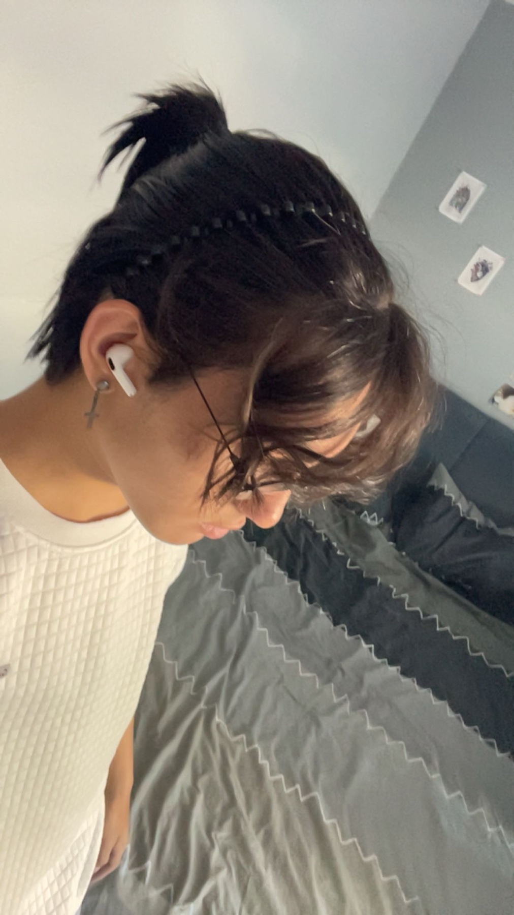 A man with dark hair styled with braids and a ponytail. He is wearing glasses and earbuds.