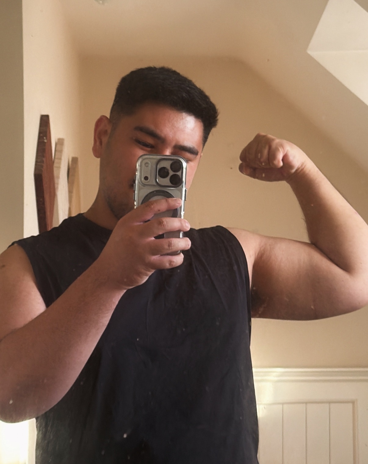 A man flexes his bicep in a mirror selfie. He is shirtless and appears to be in good shape.