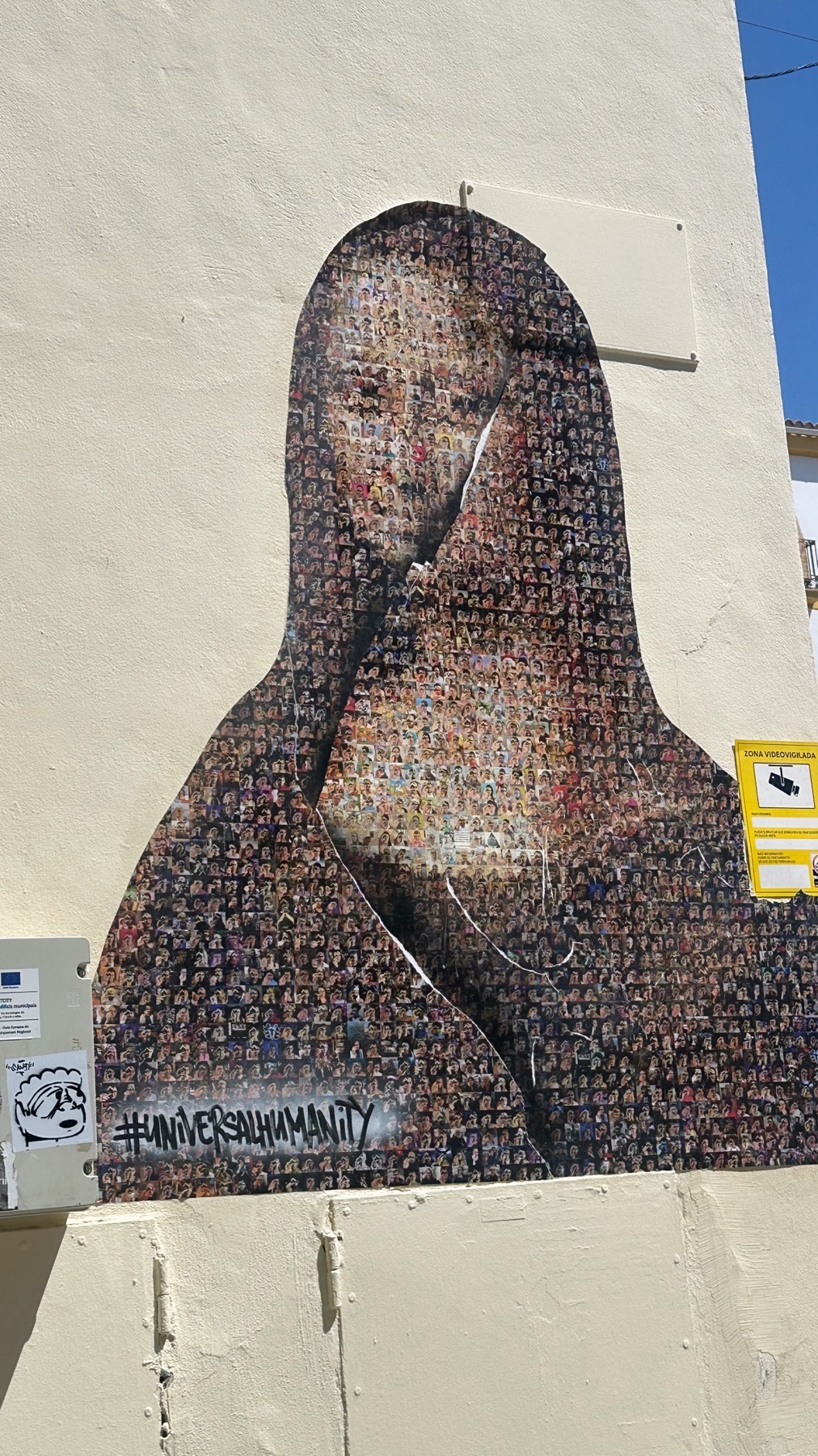 A mosaic of the Mona Lisa is displayed on a building's exterior wall. The artwork is composed of numerous small images, forming a larger portrait.