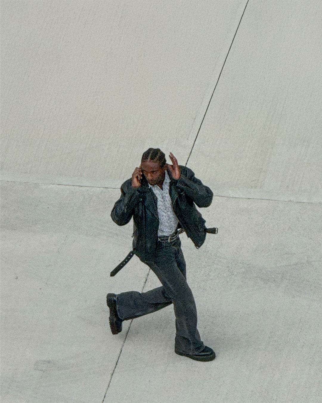 A man in a leather jacket runs while talking on the phone. The photo is taken from a high angle, giving a unique perspective.