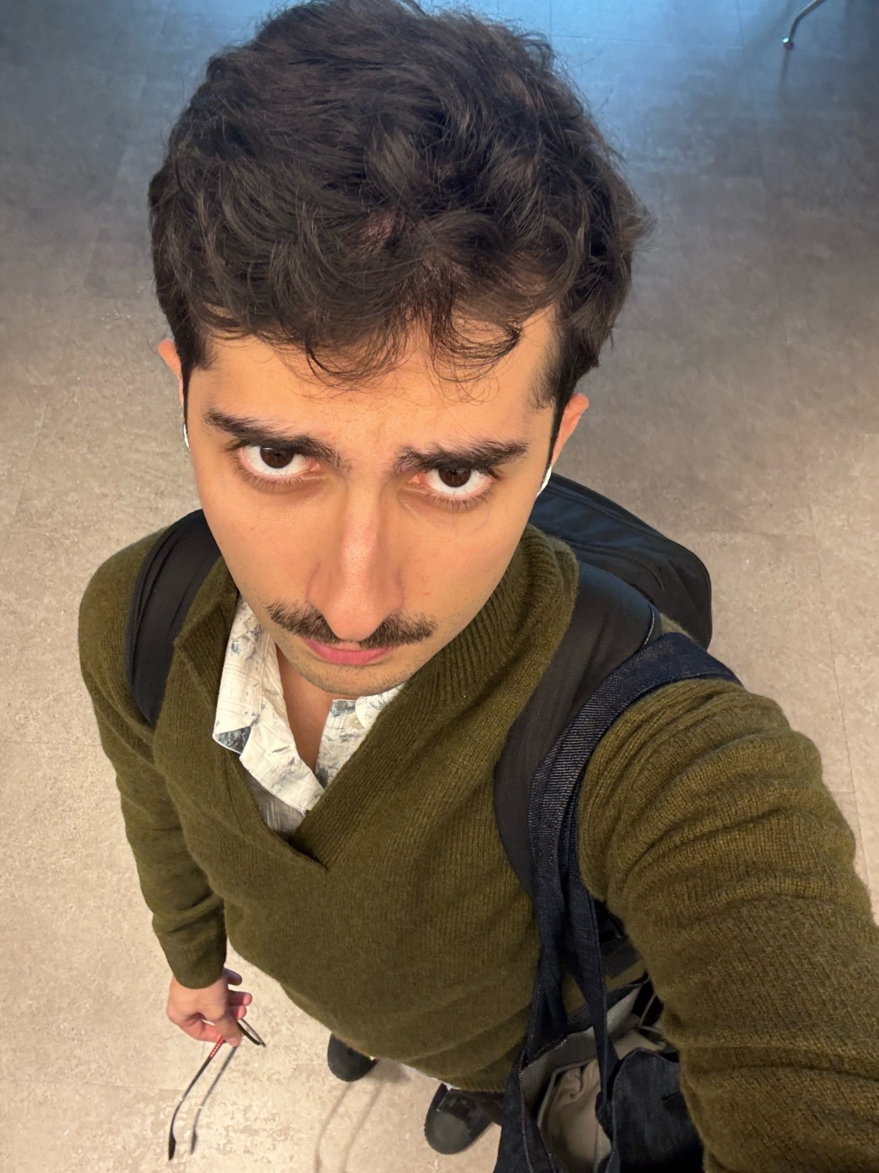 A selfie of a man looking at the camera. He is wearing a green sweater and has curly hair.