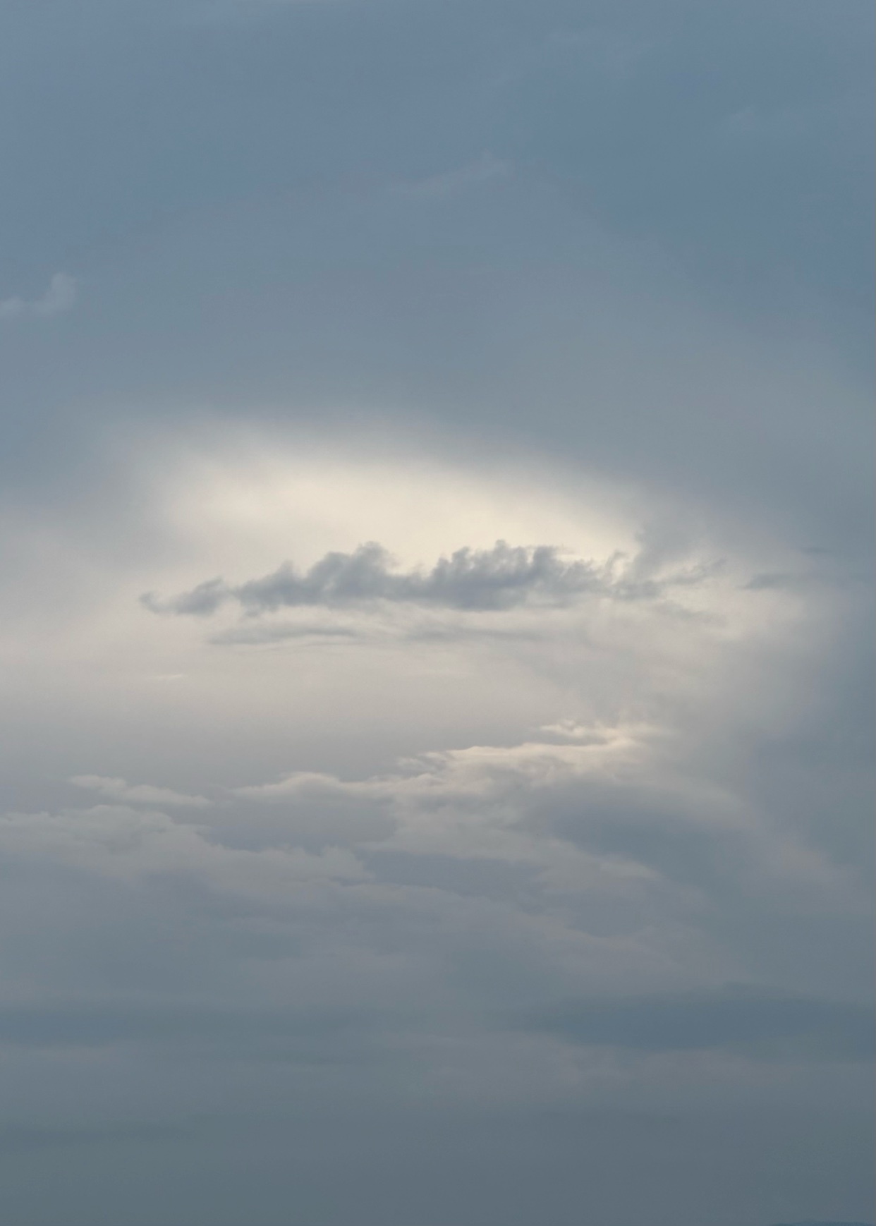 A cloudy sky with a bright spot in the center. The clouds are a mix of gray and white.