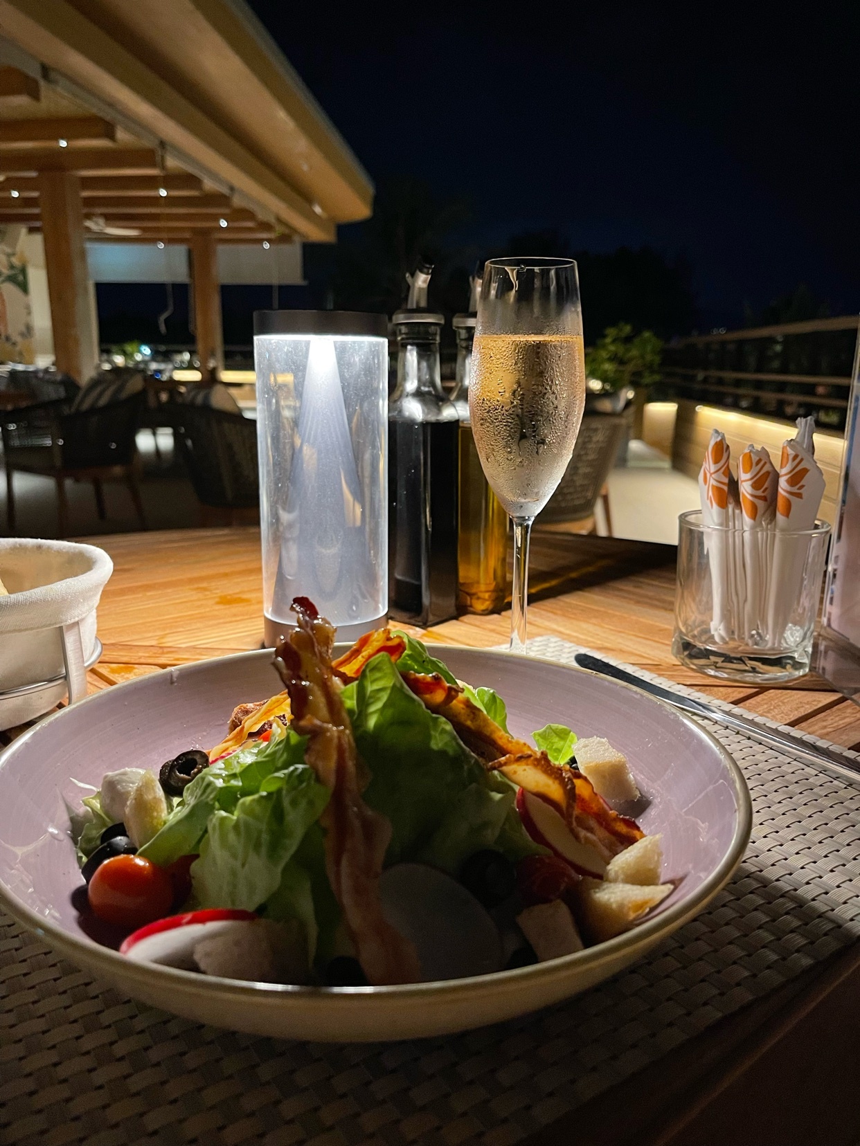 A beautifully presented salad with a glass of wine on a table at a restaurant. The photo is taken at night.