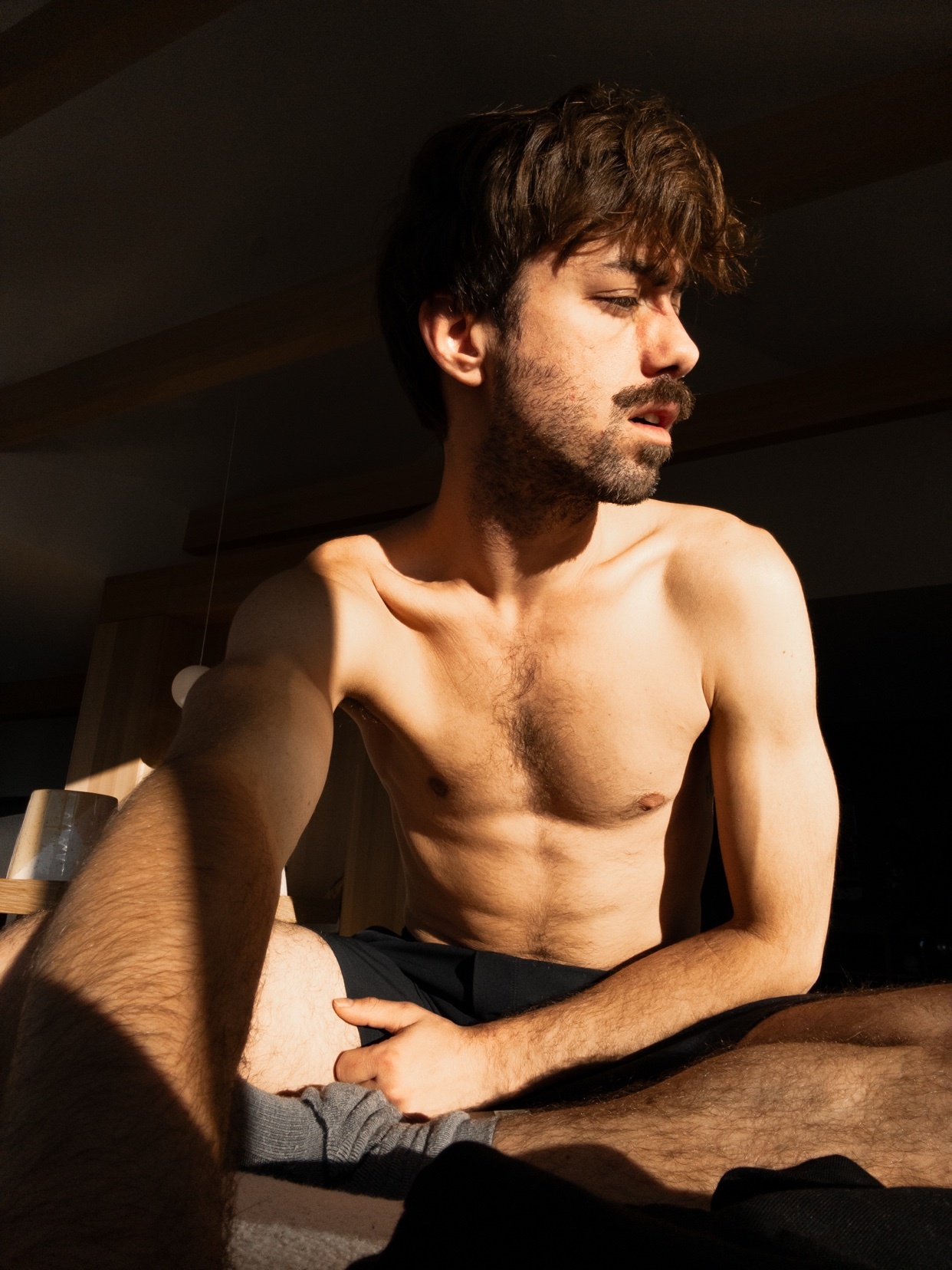 A shirtless man poses in the morning light. The photo is taken indoors, likely in a bedroom.