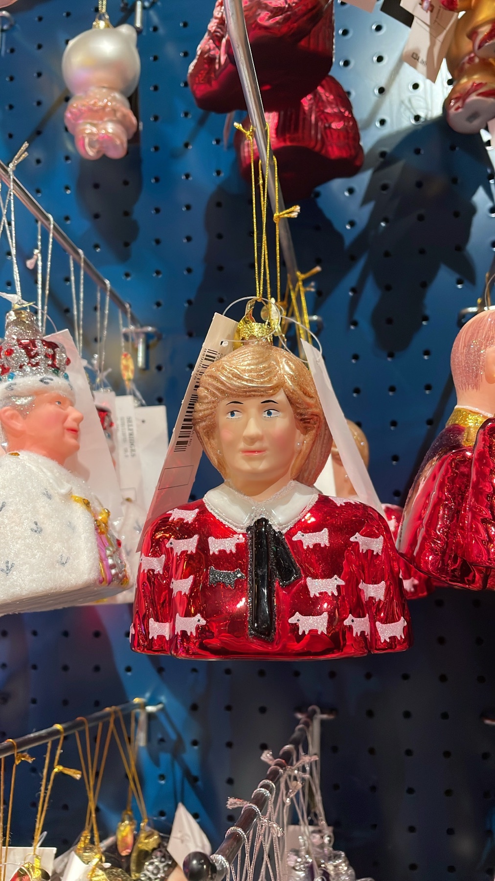 A close-up shot of a Princess Diana Christmas ornament. The ornament is red with a white collar and a black bow.