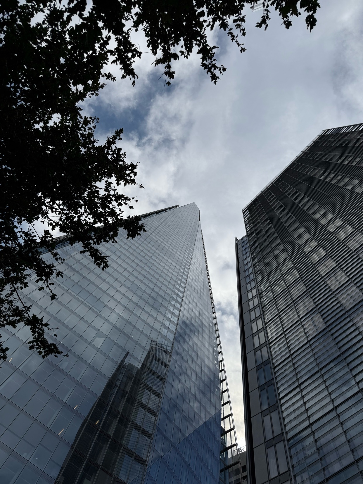A low-angle shot captures the towering skyscrapers against a cloudy sky. The buildings' glass facades reflect the sky and surrounding environment.