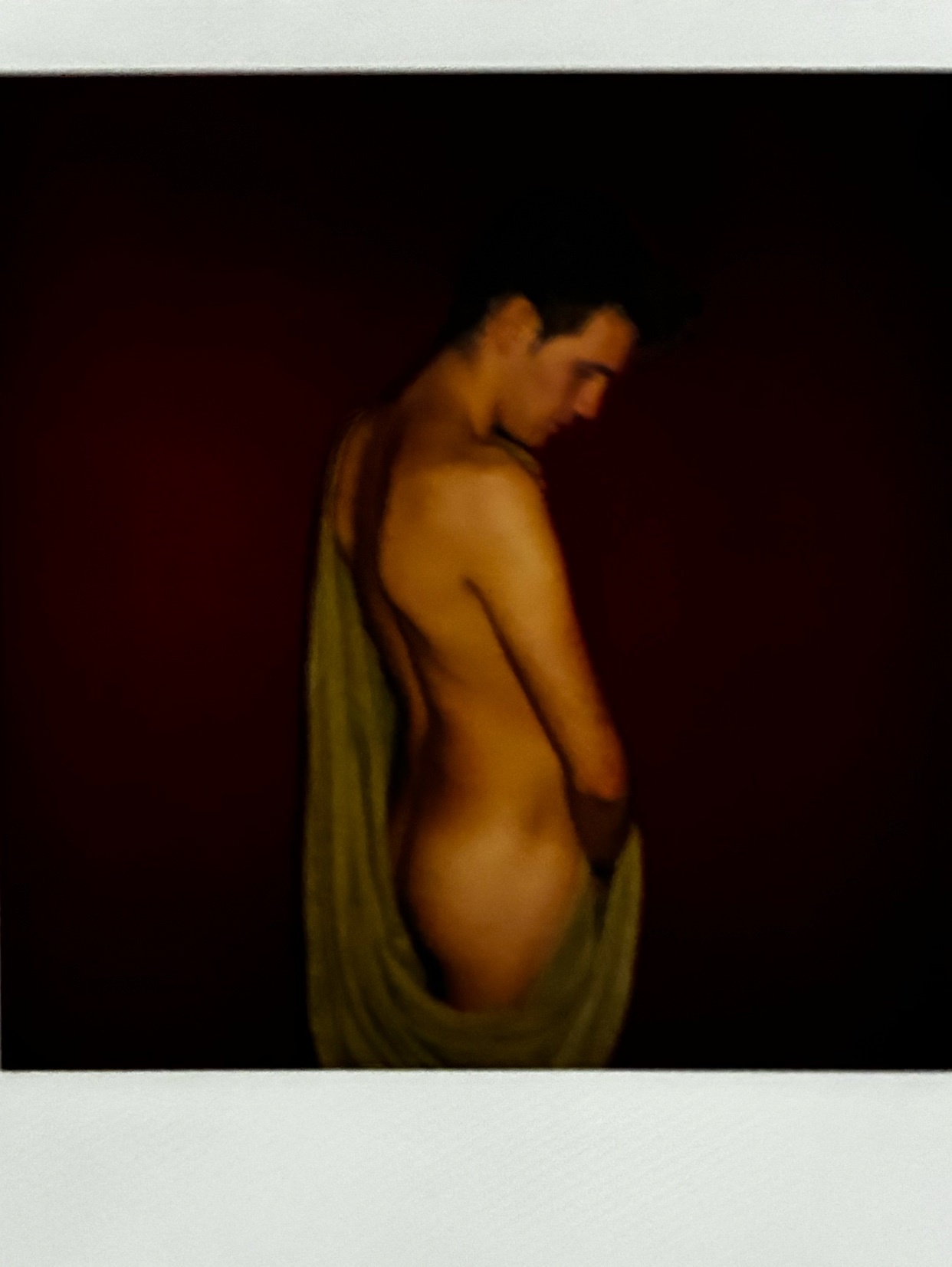 A man is captured in a studio shot, partially nude and draped in fabric. The image has an artistic and aesthetic quality.