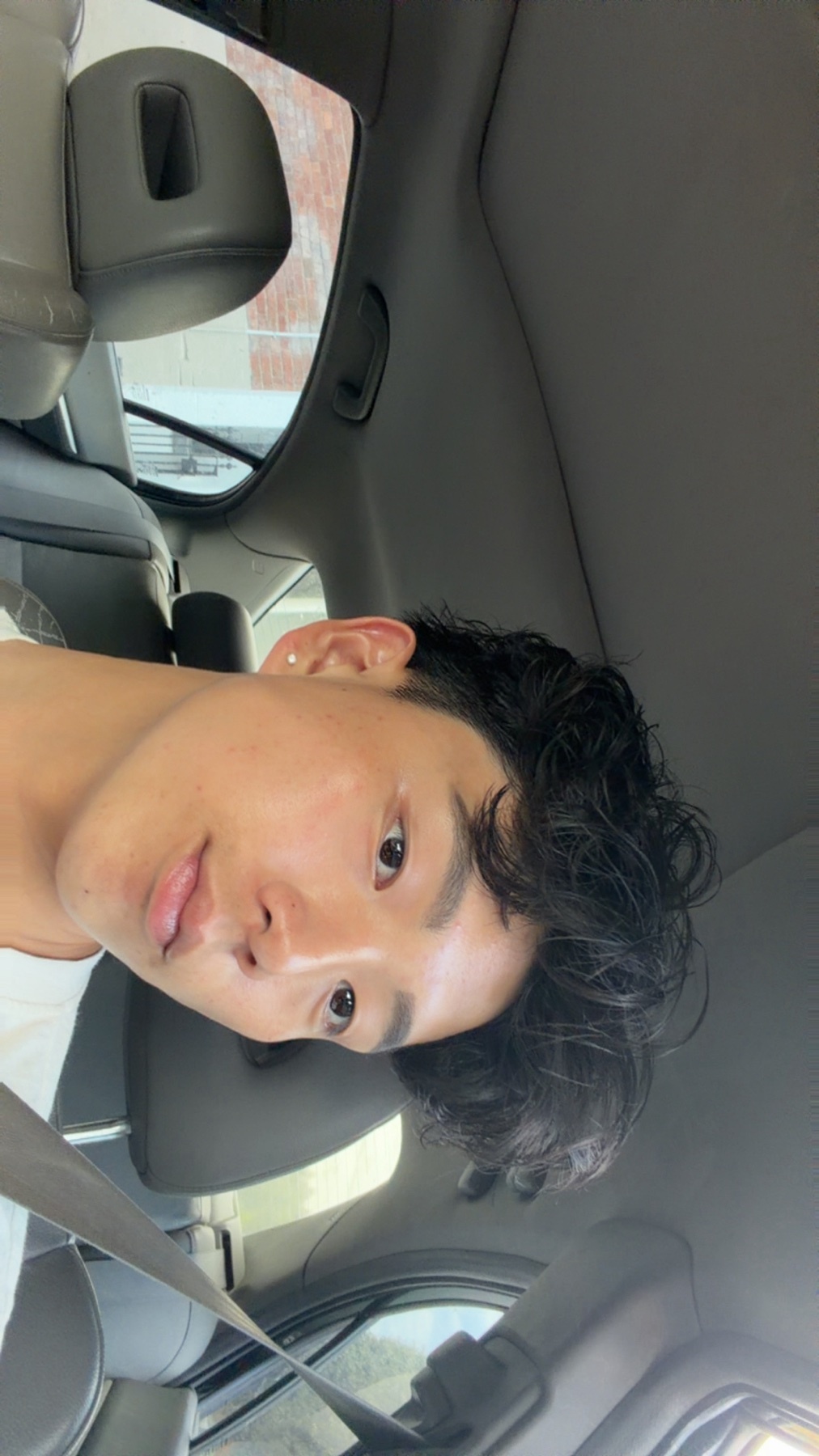 A man with curly hair takes a selfie in a car. The photo is a close-up of his face.