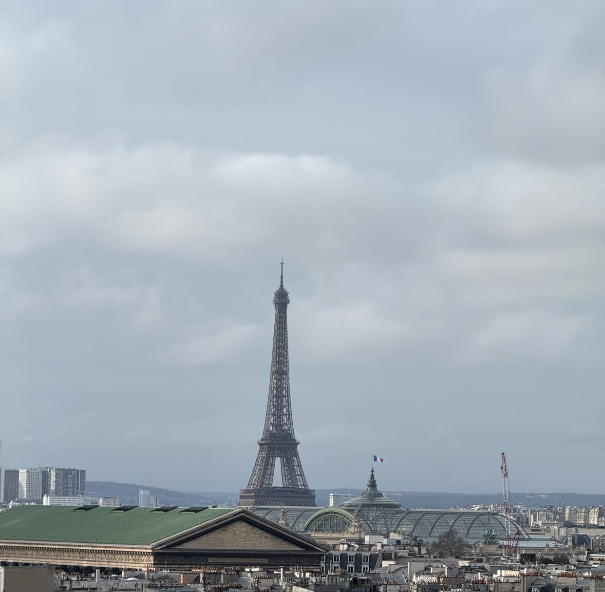 A scenic view of the Eiffel Tower in Paris, France, under a cloudy sky. The photo captures the iconic landmark amidst the cityscape.