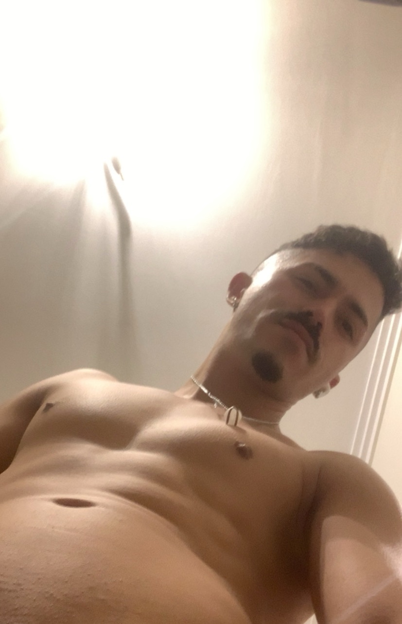 A shirtless man looks down at the camera. He has dark hair and a mustache.