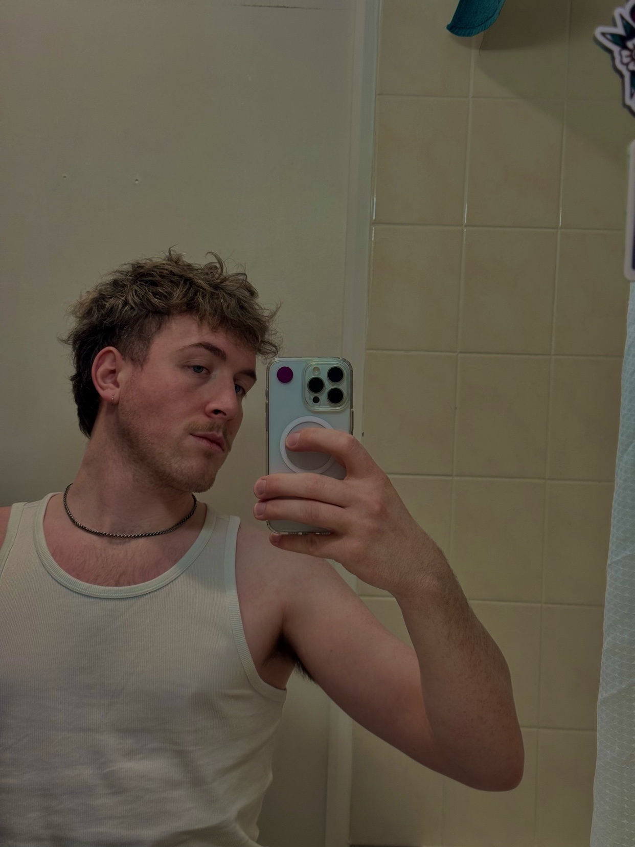 A man with curly hair takes a selfie in a tank top, looking into the camera.