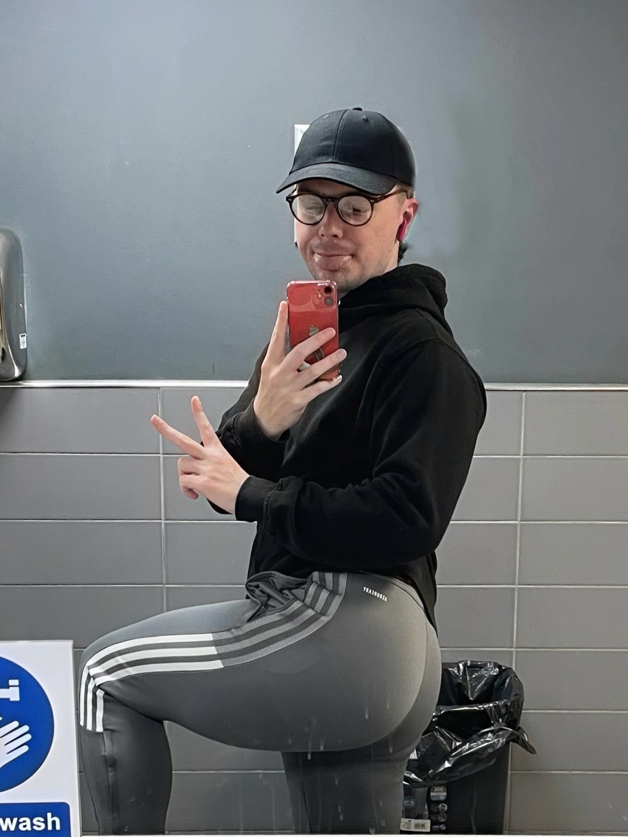 A man poses in a gym mirror, wearing a hat and athletic wear. The photo highlights his physique.