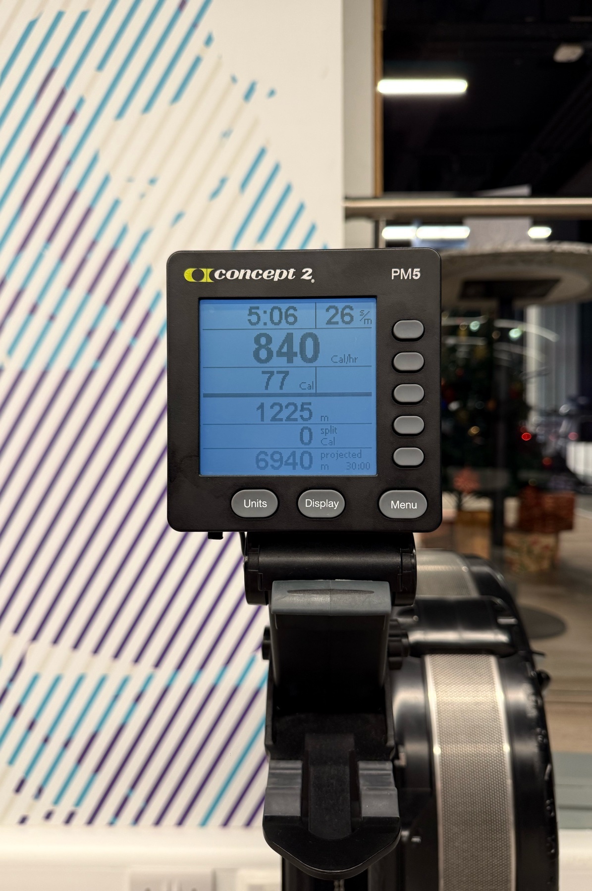 A close-up shot of a Concept 2 rowing machine display, showing workout metrics. The screen displays time, distance, and other performance data.