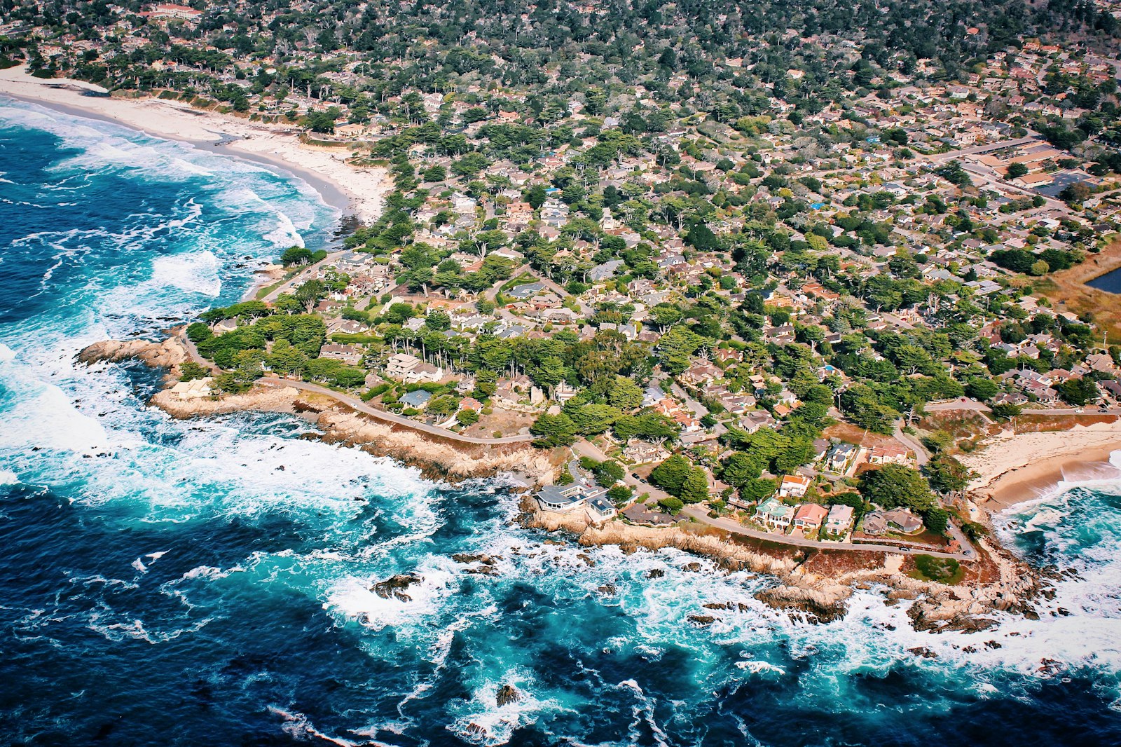Aerial along the Carmel Point coastline with surf, rocks, cypress and rooftops
