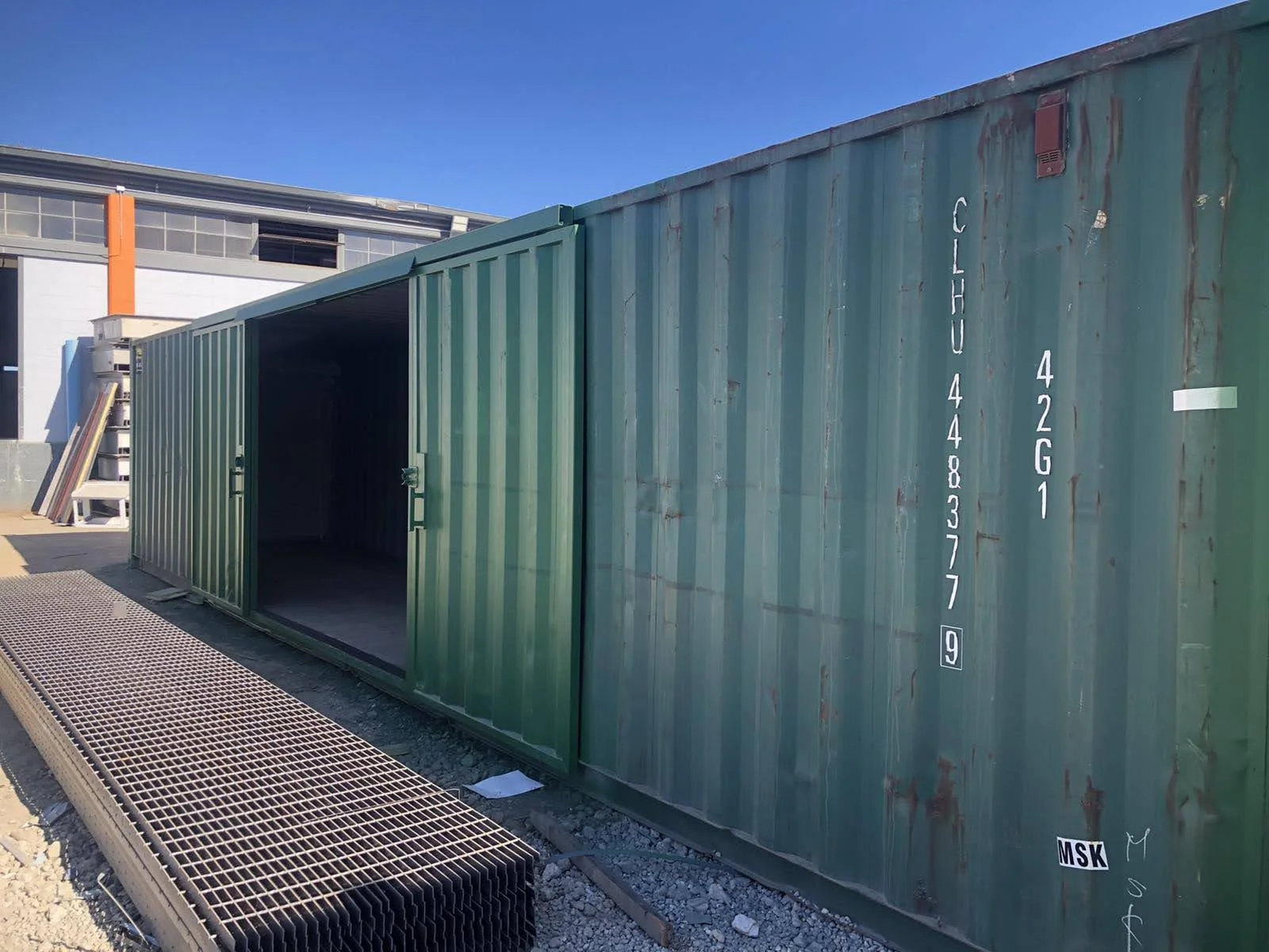 View of a shipping container with its barn doors open and corrugated flooring panels stacked outside