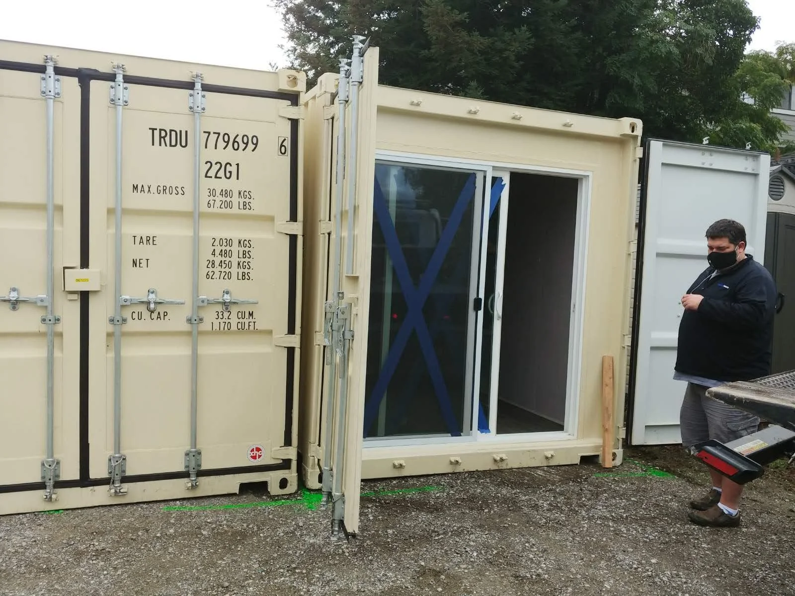 A man standing next to glass sliding doors installed behind the door of a shipping container