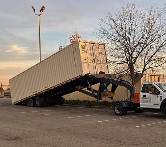 Tilt-bed truck with trailer delivering a container