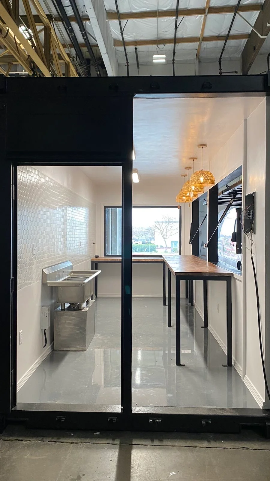 Interior of the Boba and Brew container cafe with stainless steel sink, service counter, pendant lighting, and finished walls