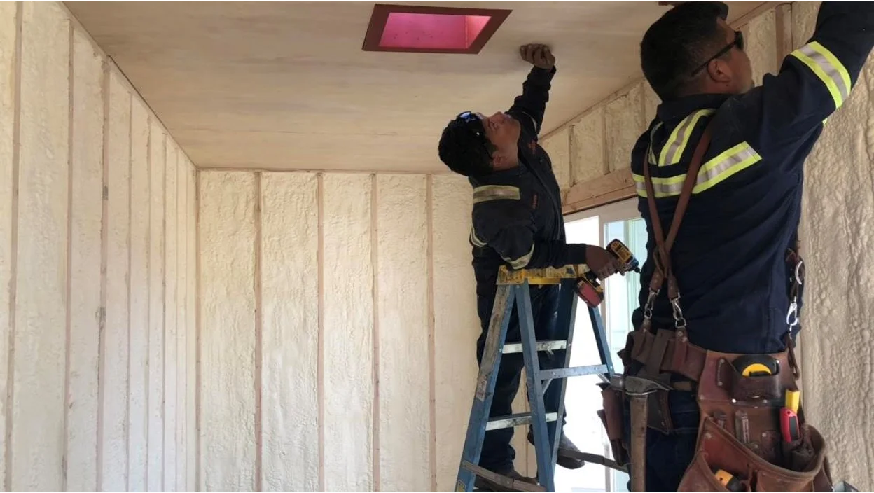 Two construction workers doing interior design work on a shipping container.