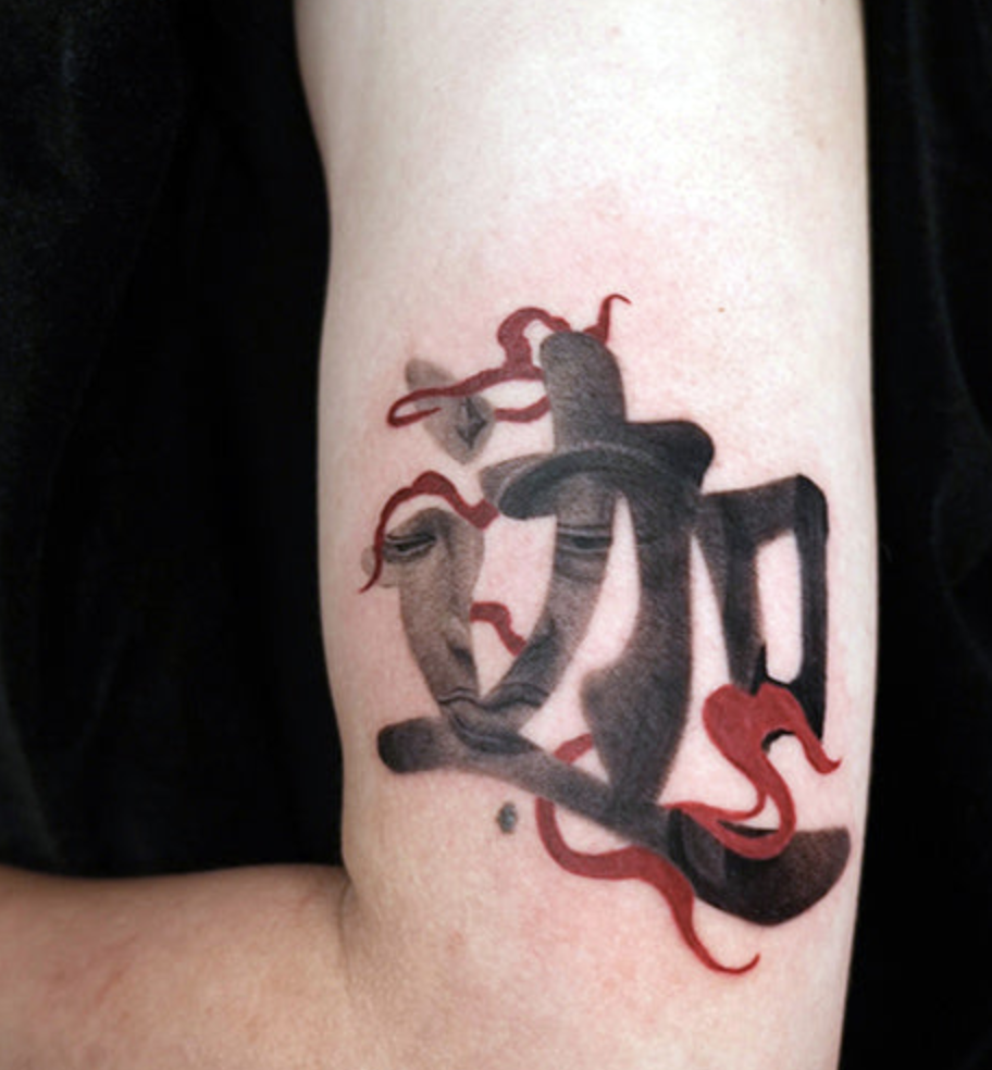 A black and grey tattoo on an arm featuring stylized, abstract calligraphy that incorporates a faint human profile within the brushstrokes, accented by wispy red smoke-like flourishes.