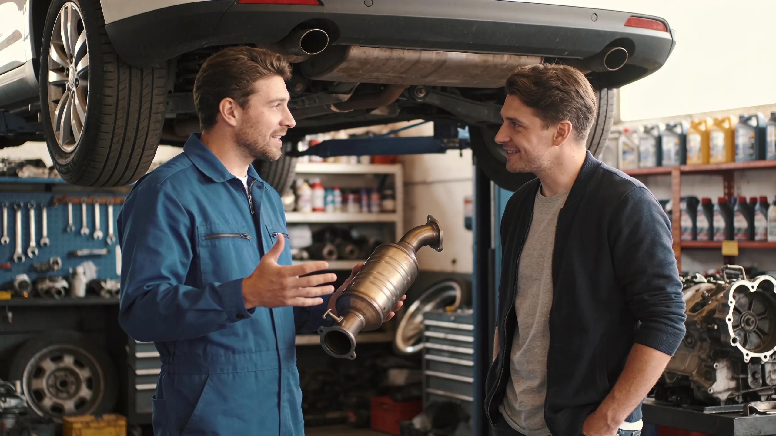 Mechanic explaining catalytic converter replacement options to a car owner in an auto repair shop Mechanic and customer discussing catalytic converter replacement at Route 40 Auto.
