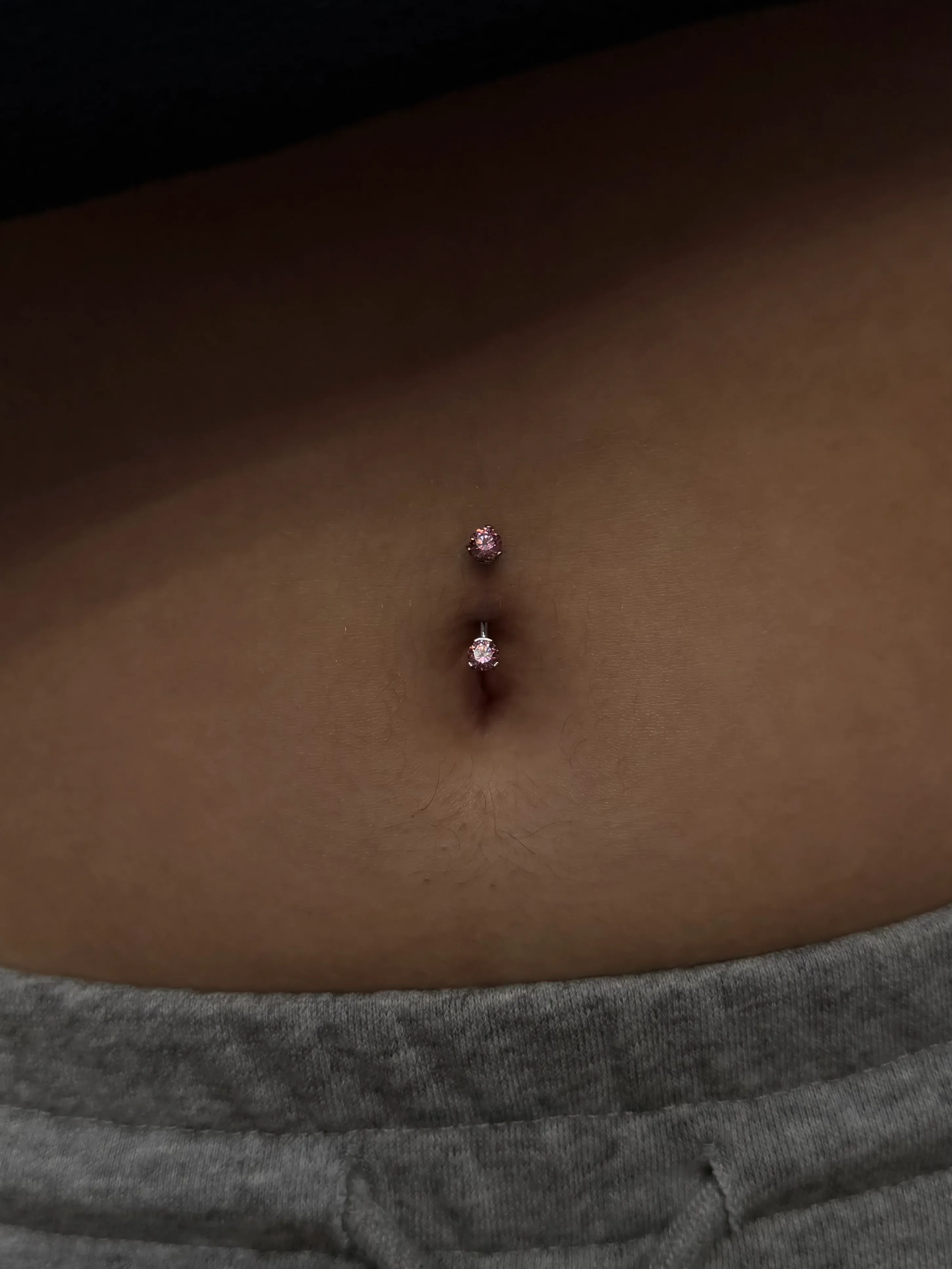 Belly button piercing featuring a silver curved barbell set with two sparkling pink gemstones.