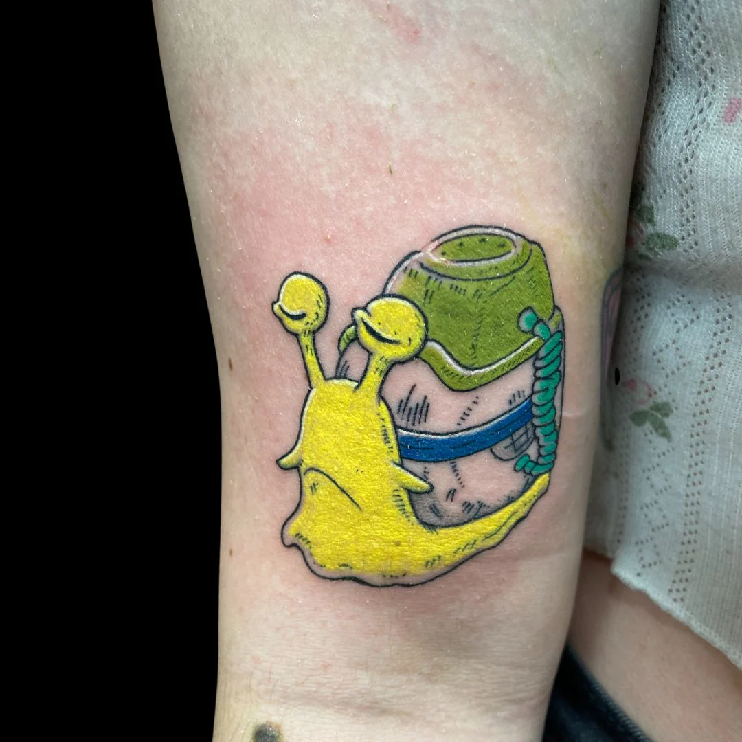 A vibrant, cartoon-style tattoo on an arm featuring a bright yellow snail with a cheerful expression, carrying a green and white cement mixer on its back.