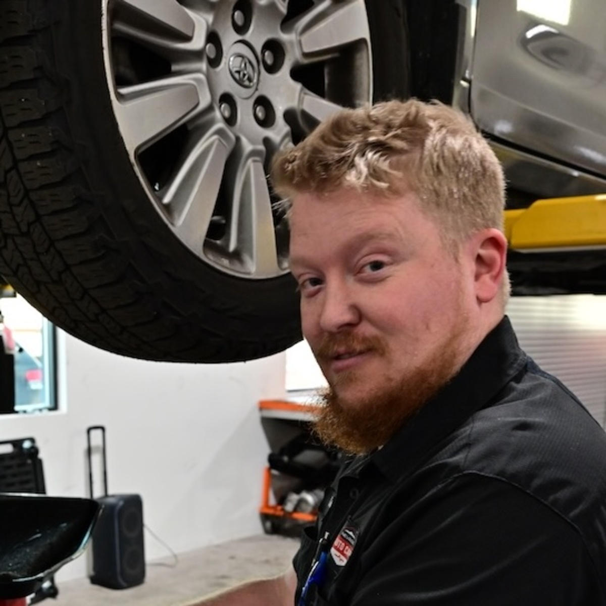 Mechanic working under a car with a raised tire and tools nearby