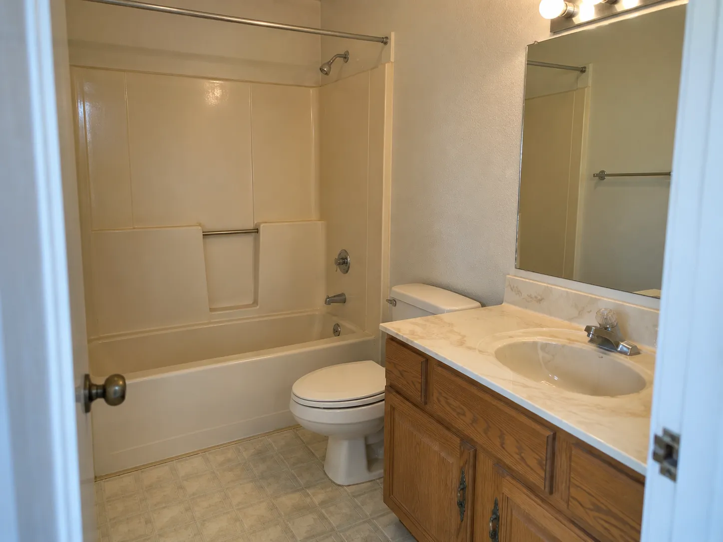 Dated condo bathroom with worn grout and an old fiberglass tub before a remodel