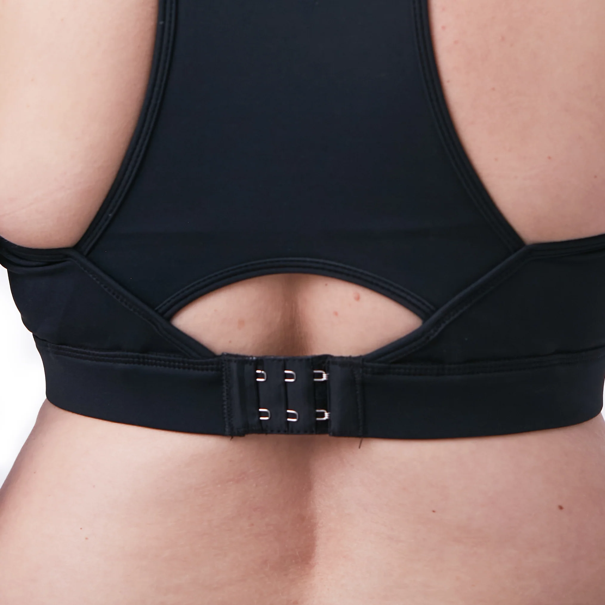 Close-up rear view of a woman wearing a black Senita nursing sports bra, highlighting the secure three-row hook-and-eye back closure, wide adjustable under-band, and breathable racerback keyhole cutout.