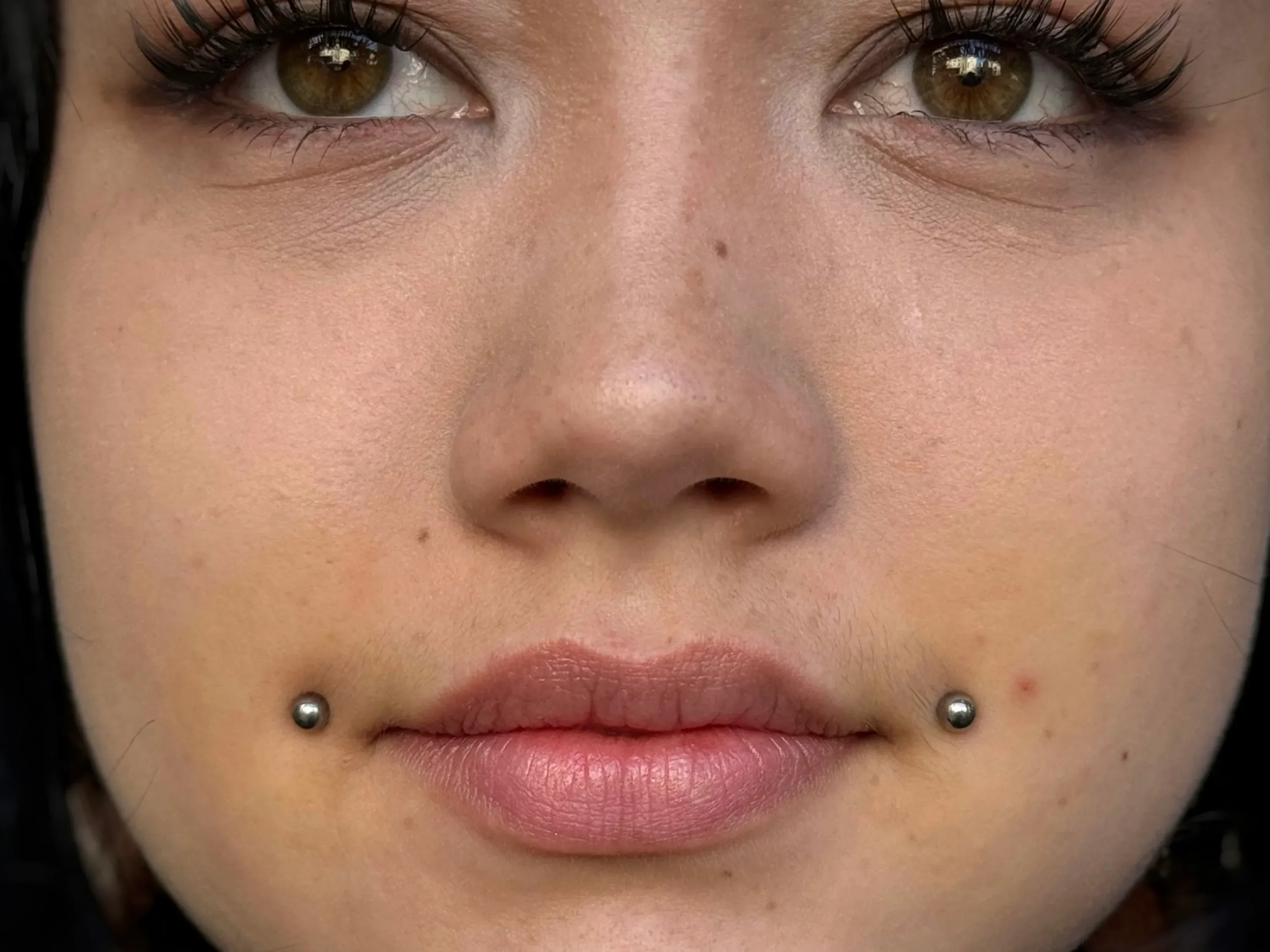 Close-up of symmetrical cheek cheek piercings with silver metallic stud ends on a woman's face.