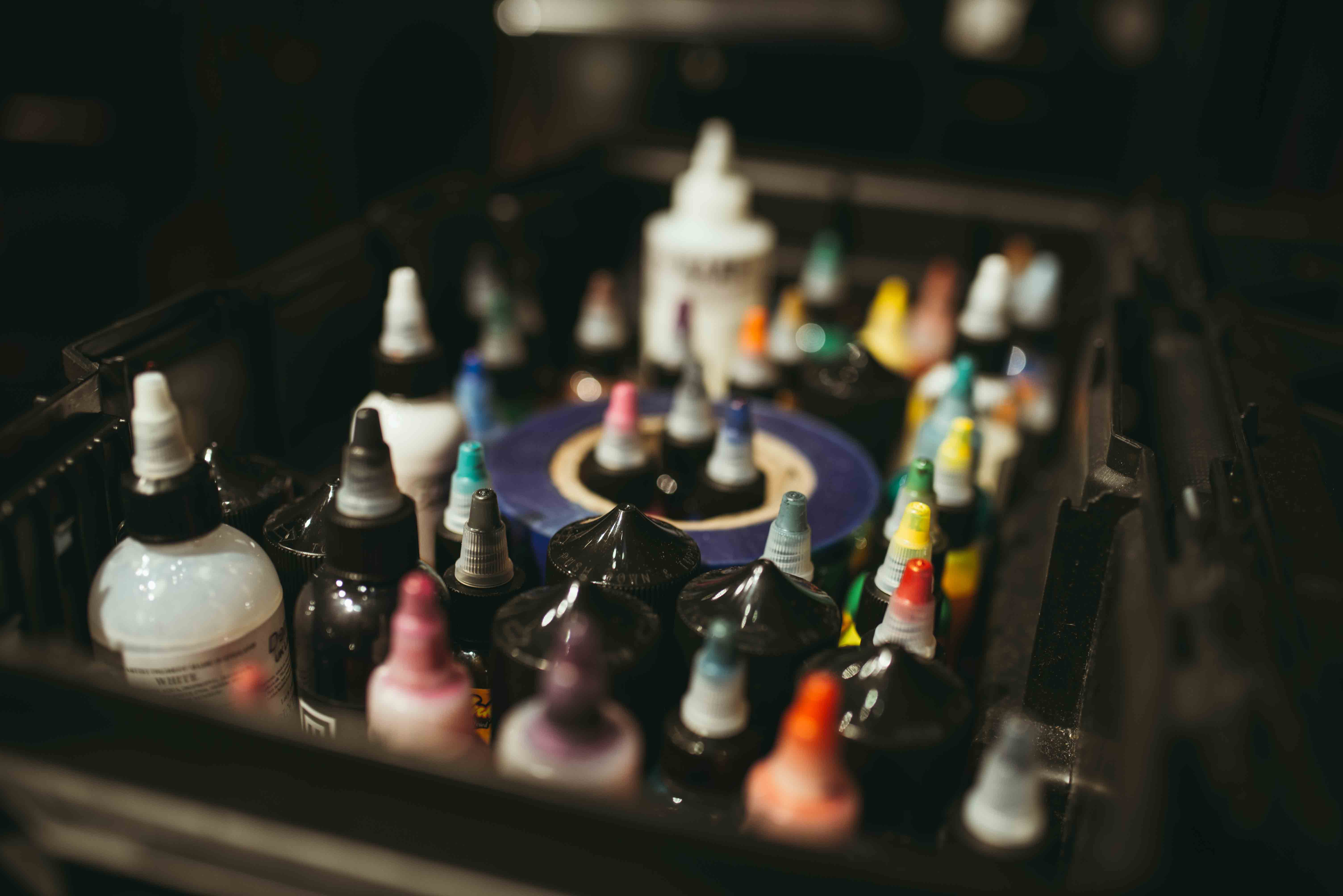 A close-up, shallow depth-of-field shot looking into an organized black workstation box filled with various bottles of colorful and black professional tattoo ink.