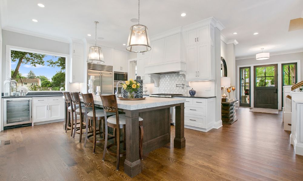 Bright luxury kitchen staged for premium Franklin houses for sale, featuring a large dark wood island with seating, white custom cabinetry, upscale stainless steel appliances, and polished hardwood flooring.