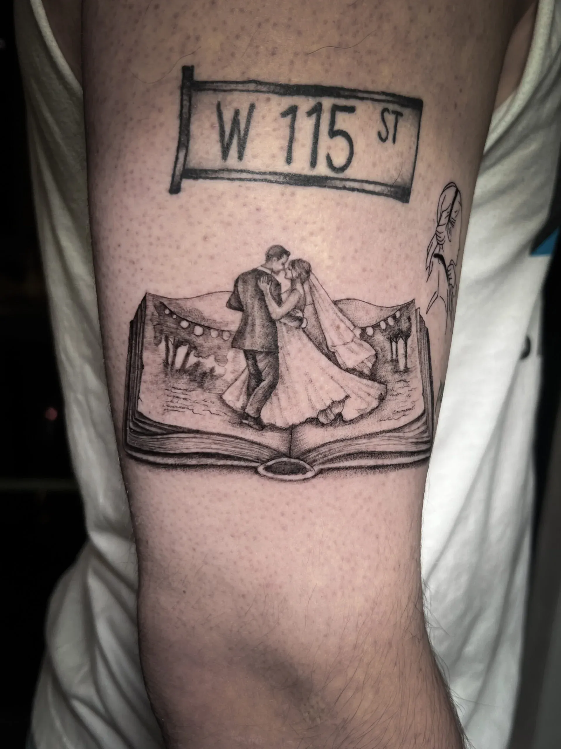 Fine-line black and grey arm tattoo of a bride and groom dancing inside an open book beneath a street sign.